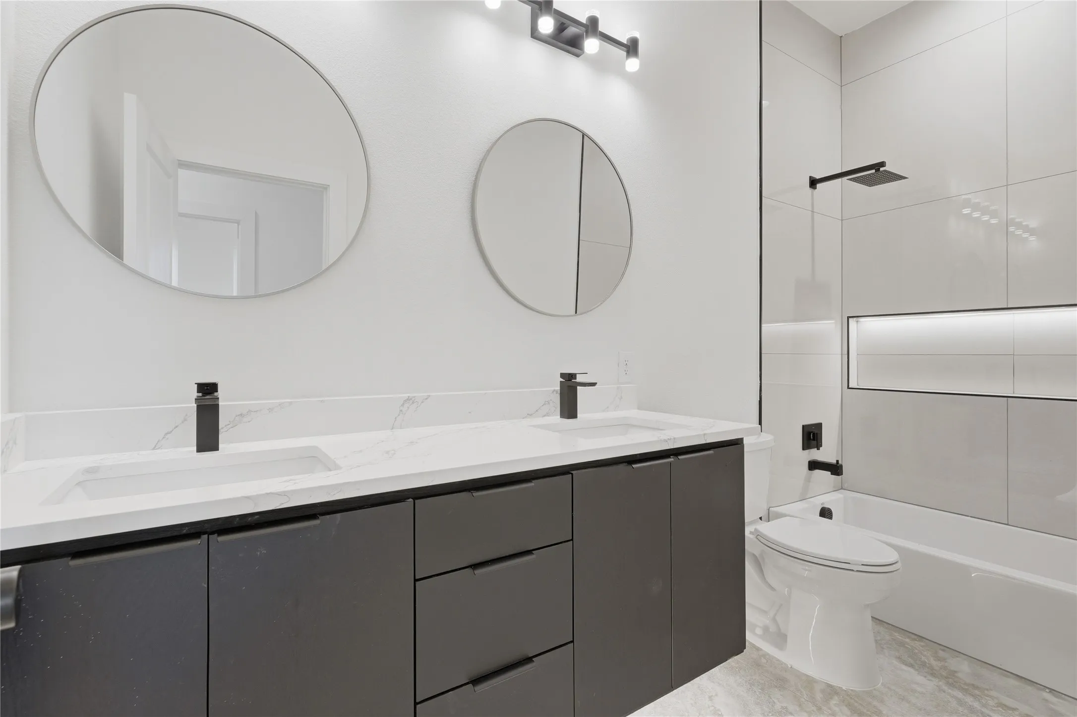 Contemporary bathroom featuring a dual vanity with white countertops and dark cabinetry, two round mirrors, and black matte fixtures