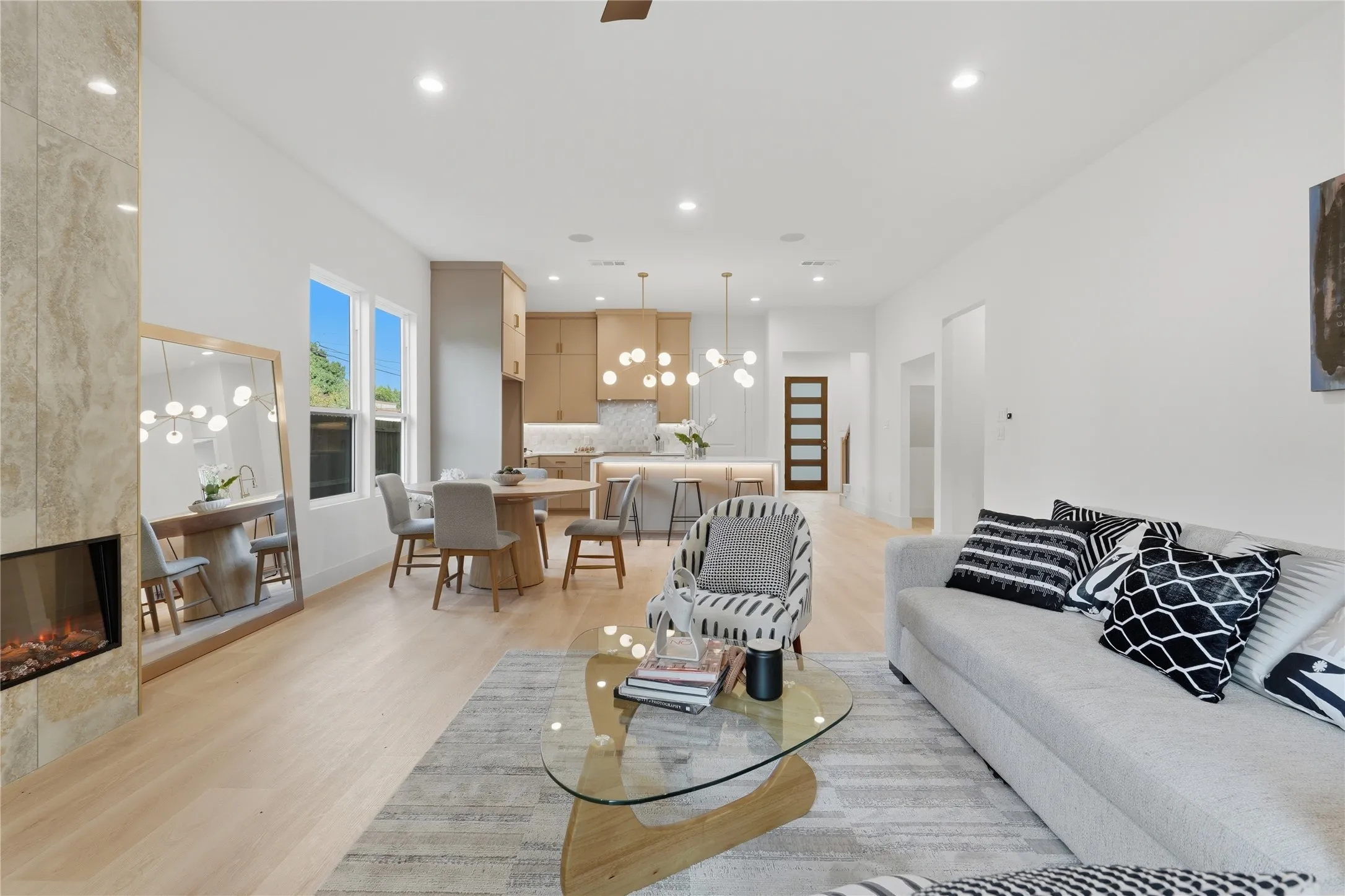 Open-concept living area featuring light wood-finish flooring, a stone-clad fireplace with a modern insert, recessed lighting, and a defined dining space with contemporary pendant lighting