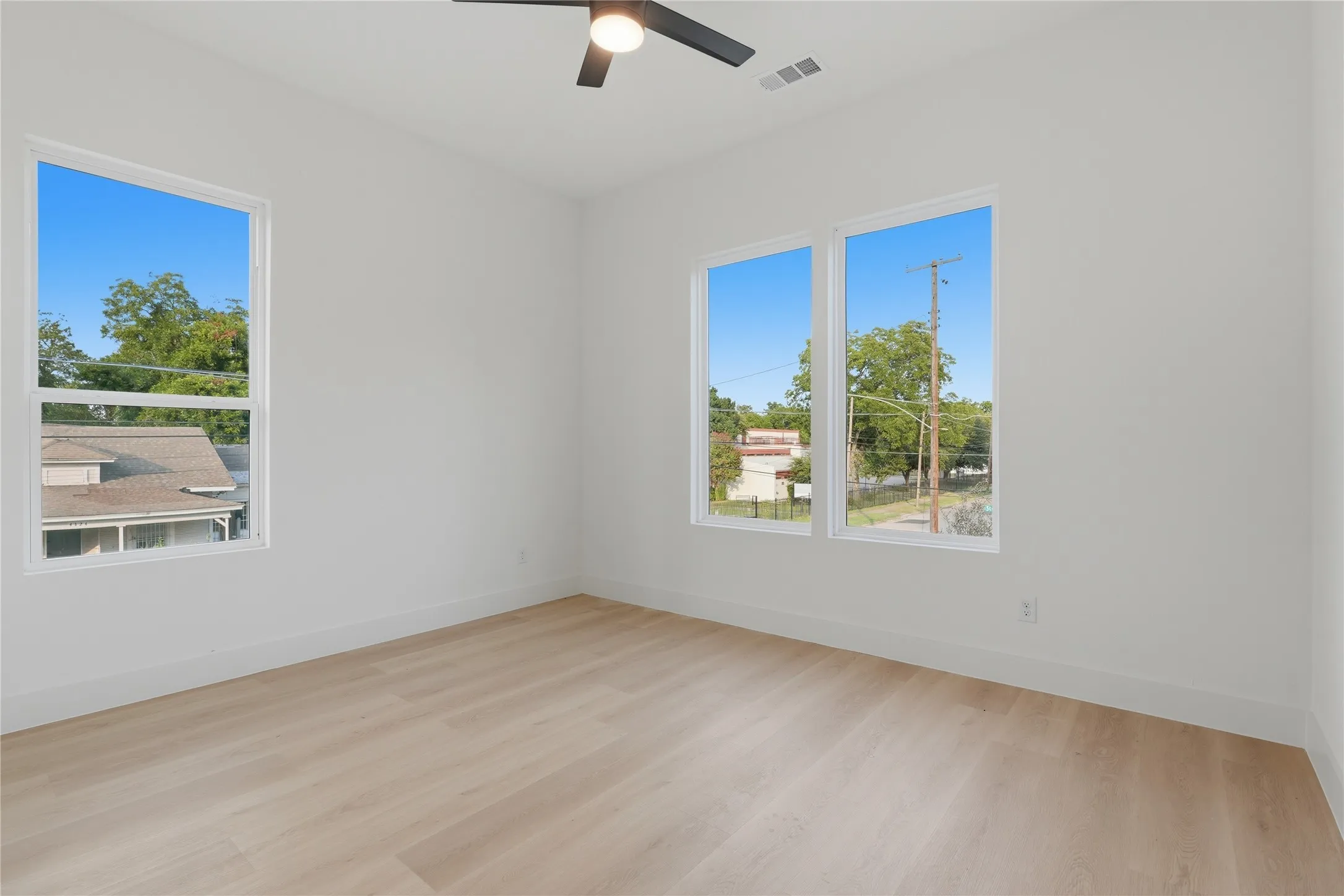 Bright room featuring a contemporary ceiling fan, three windows with white frames, clean white walls, and light wood-finish flooring