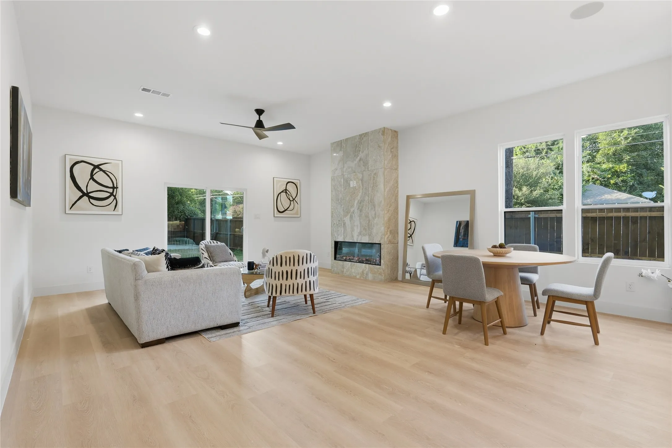 Open-concept living space featuring wood-finish flooring, recessed lighting, and a modern fireplace with a stone surround