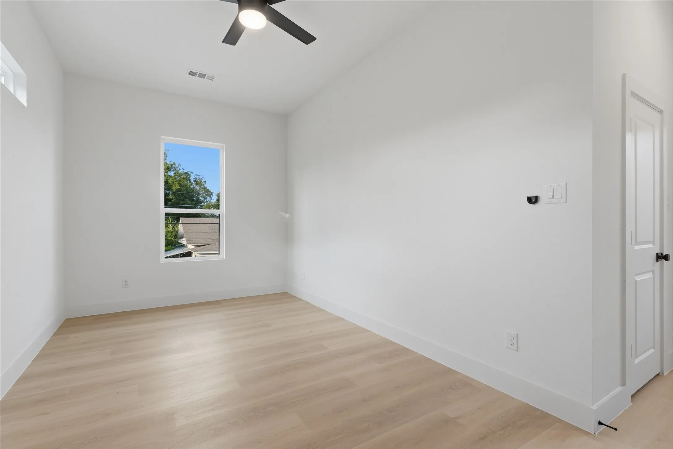 Room featuring light wood-finish flooring, white walls, and a modern ceiling fan