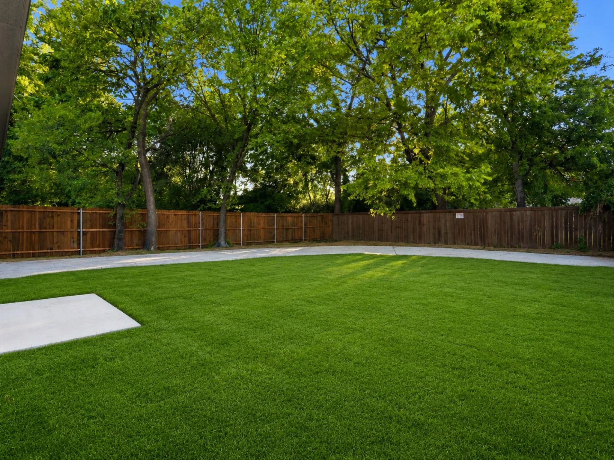 Expansive backyard featuring a lush lawn, mature perimeter trees, a full privacy fence, a concrete patio, and a concrete pathway