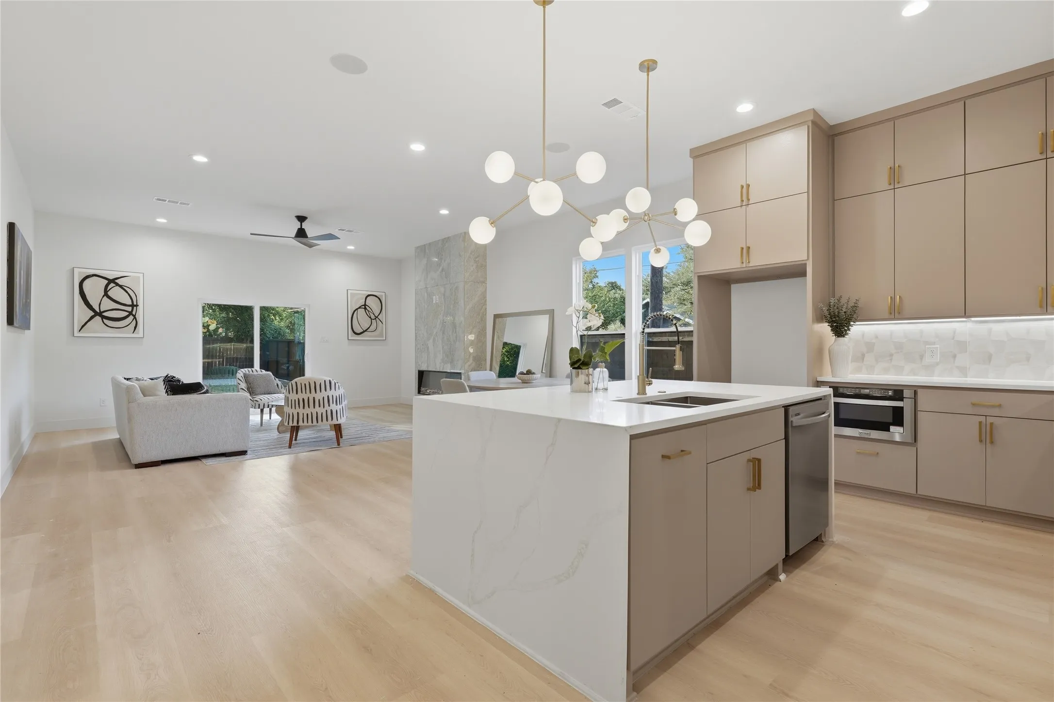 Open-concept living space featuring a central kitchen island with a waterfall countertop, integrated sink, and modern pendant lighting