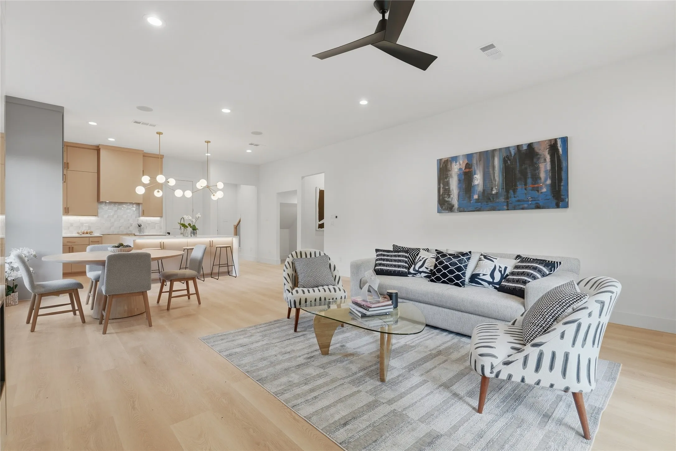 Open-concept living space featuring light wood-finish flooring, recessed lighting, a modern ceiling fan, and a kitchen with light wood cabinetry and a pendant lighting fixture