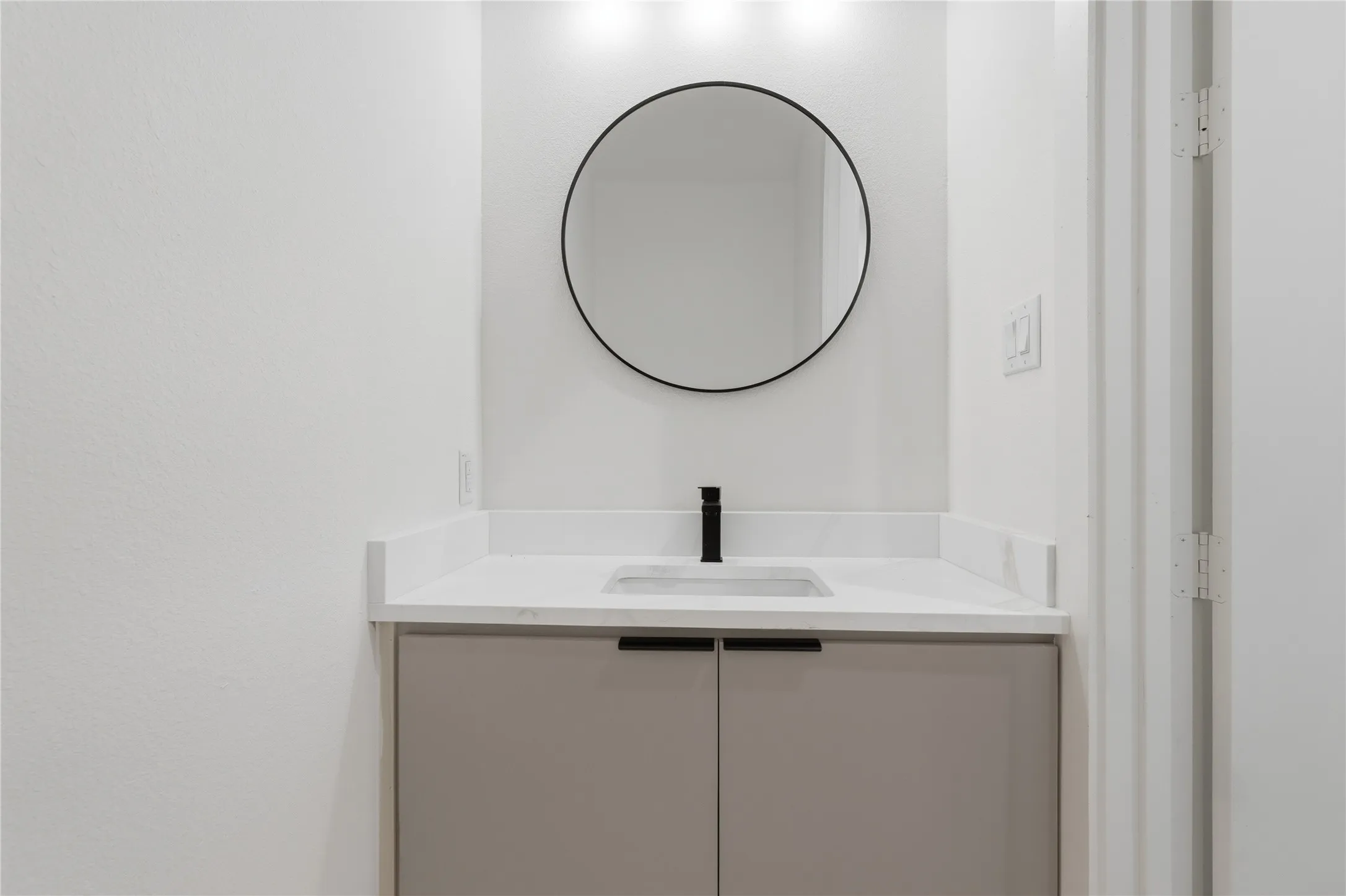 Modern vanity featuring a light gray cabinet, white countertop with integrated sink, and a matte black faucet