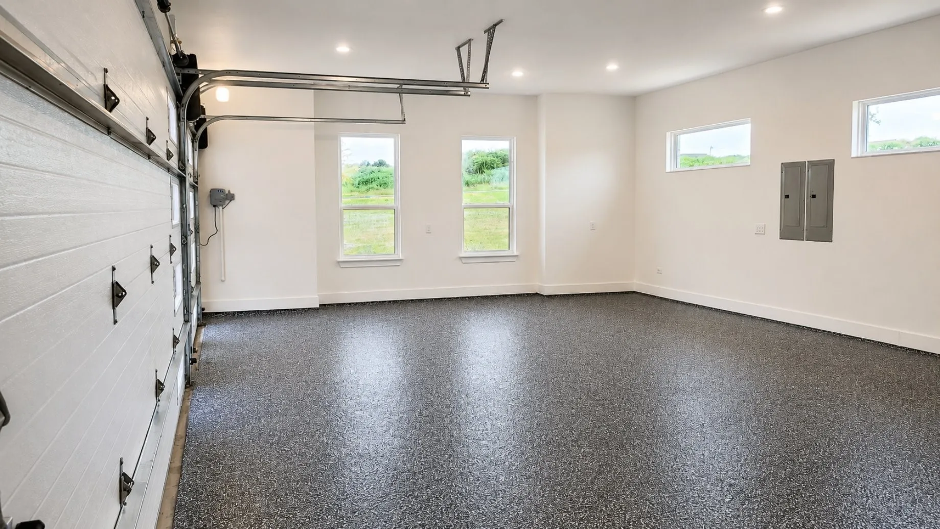Spacious garage featuring a durable epoxy-coated floor, bright recessed lighting, multiple windows providing natural illumination, and an insulated, wind resistant garage door