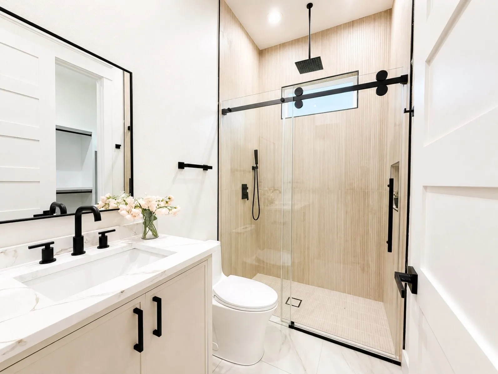 Modern guest quarter bathroom featuring a single vanity with a white countertop and rectangular sink, black fixtures, and a frameless glass shower enclosure