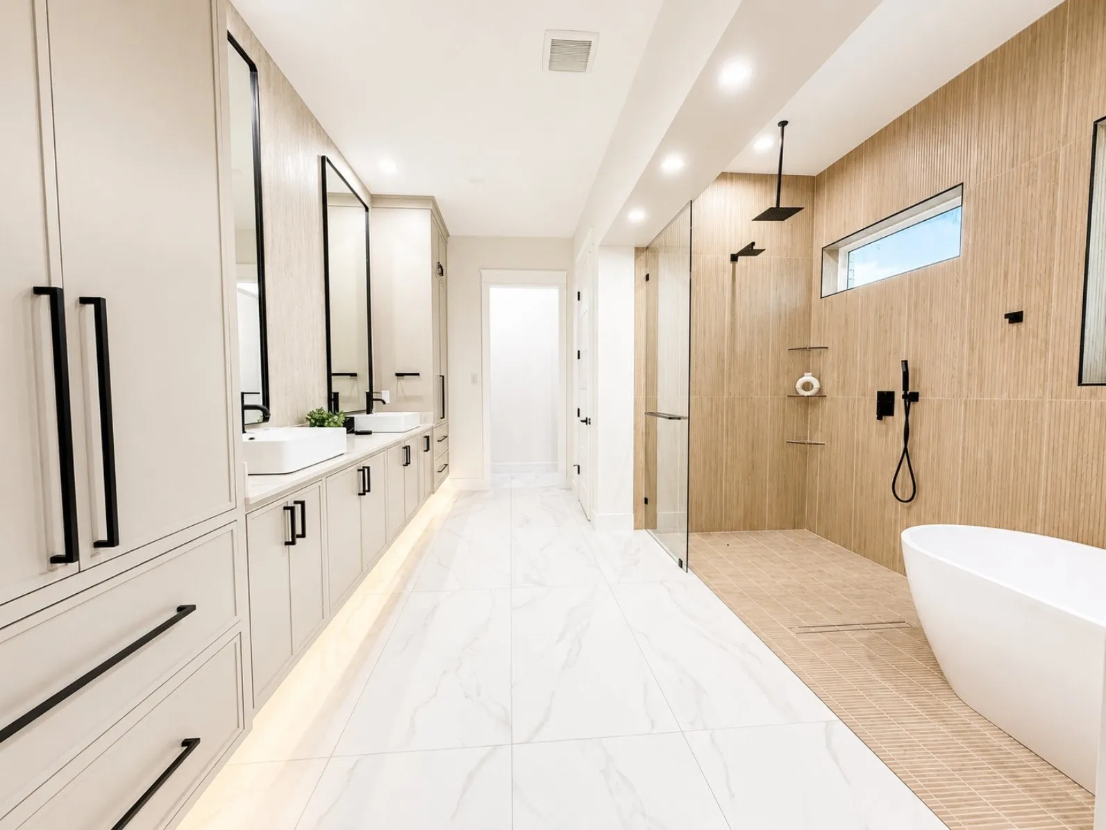 Spacious bathroom featuring dual vessel sinks, extensive cabinetry with matte black hardware, a frameless glass shower enclosure with a rain shower head, a freestanding soaking tub, and large format tile flooring