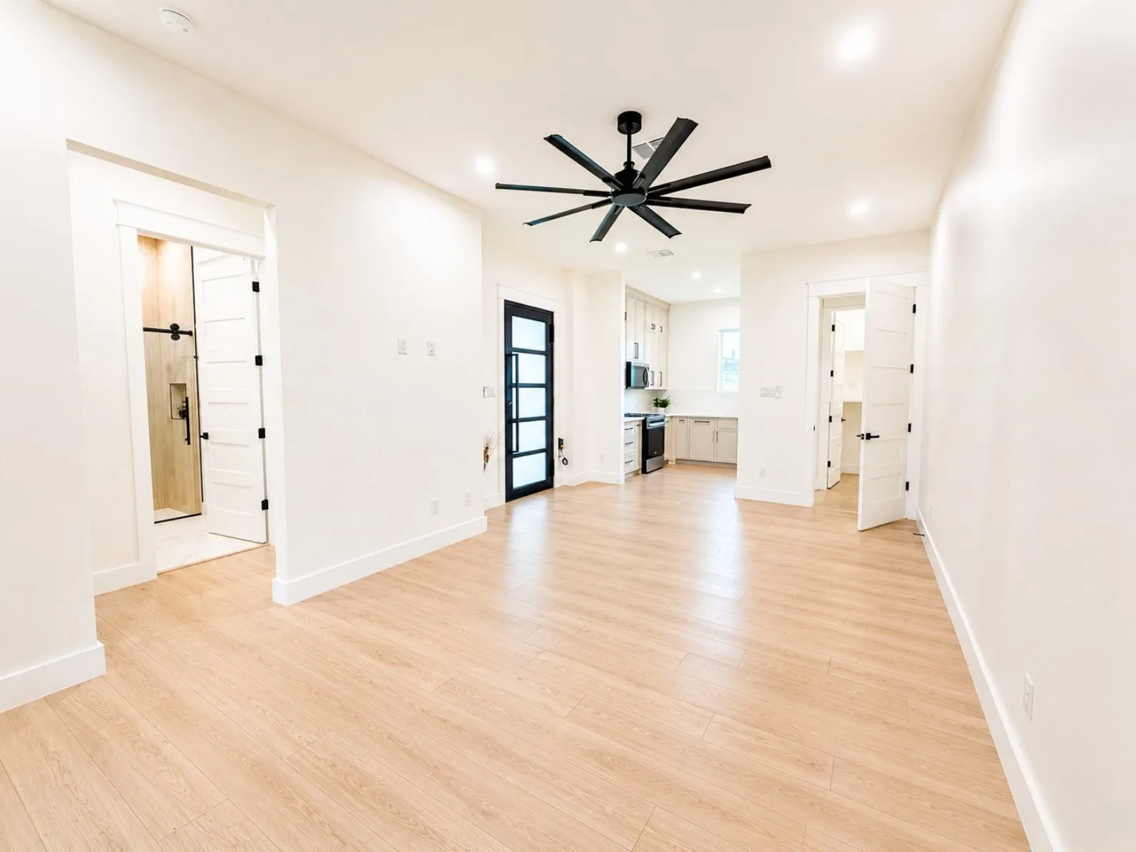 Bright guest quarter living space featuring light wood-finish flooring and a contemporary black ceiling fan
