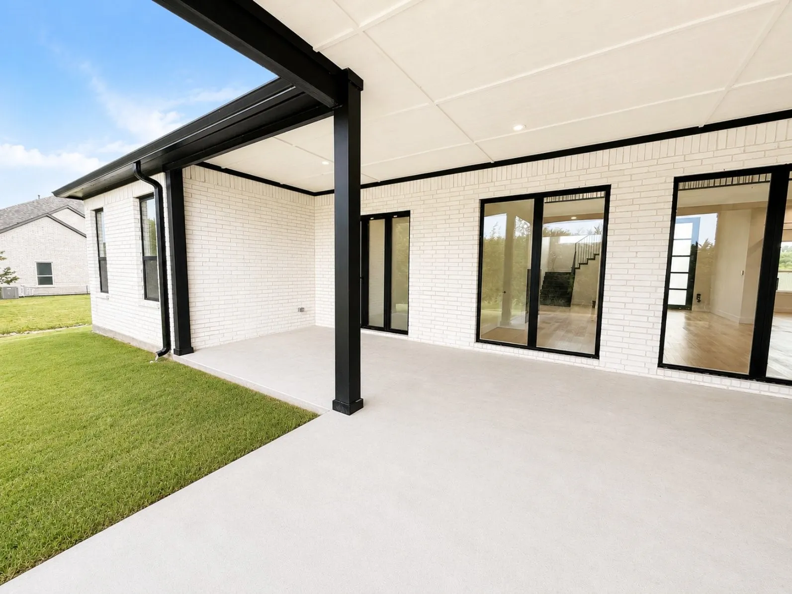 Covered concrete patio featuring white brick exterior walls and black-framed glass windows and foldable door