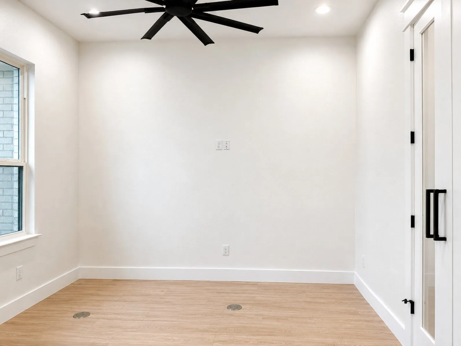 Spacious interior room featuring wood-finish flooring, white baseboards, and a contemporary ceiling fan