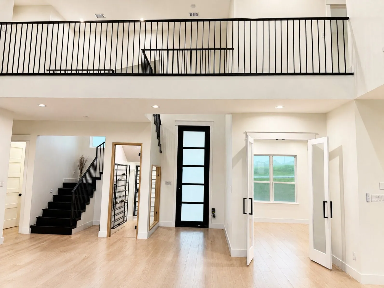 Two-story entry featuring light wood-finish flooring, a black geometric staircase with metal railing, an open upper-level landing with matching railing, recessed lighting, and a black paneled front door