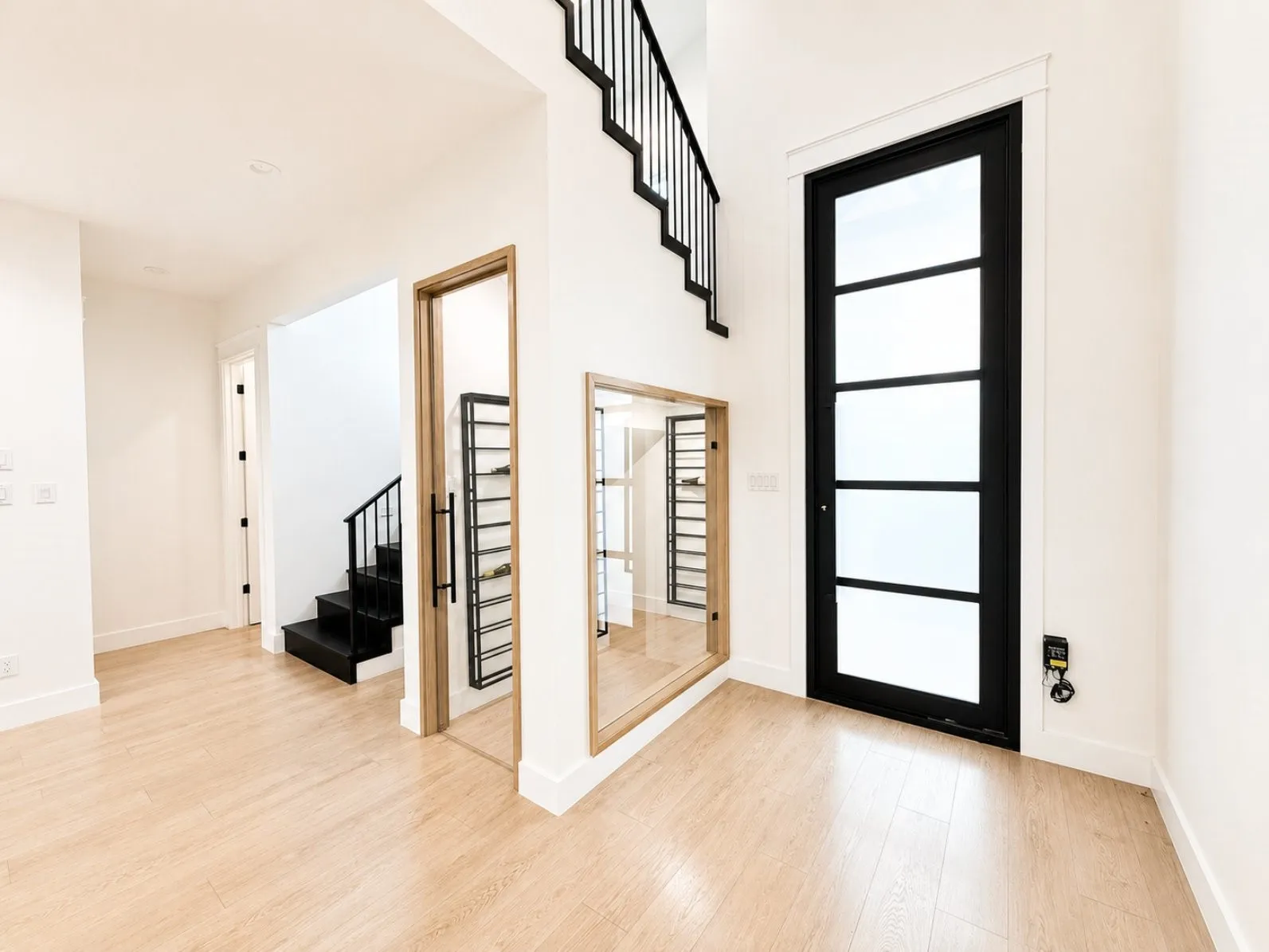 Foyer featuring a tall black-framed entry door with frosted glass panels, light wood-finish flooring, and a contemporary black metal stair railing