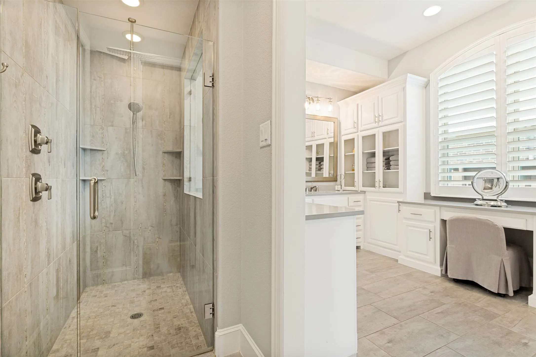 The primary bath includes a large shower with a floor tile surround and a frameless glass enclosure.  Two sets of corner shelves area available for shampoos and other bath products.  Ceramic tile is on the floor of the bath and recessed lights are above.