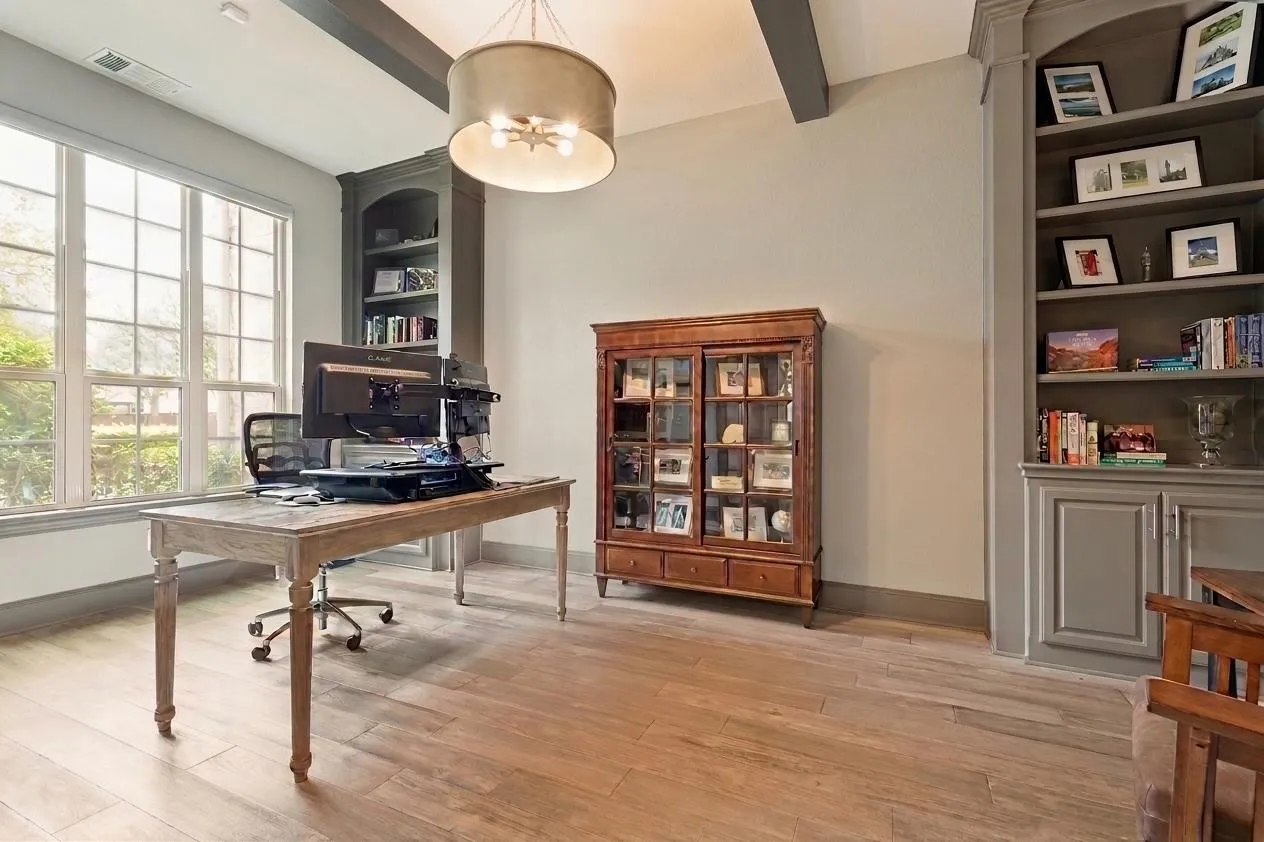 This study will definitely wow you!  Flooded with light through three windows with shades, the room is ideal for comfortably working from home.  Three bookcases in the room - with the third across from the one by the windows - provide considerable storage, and matching beams accent the ceiling.  The light Luxury Vinyl Plank floors are a nice contrast.  A modern chandelier is above and double doors provide privacy when working.