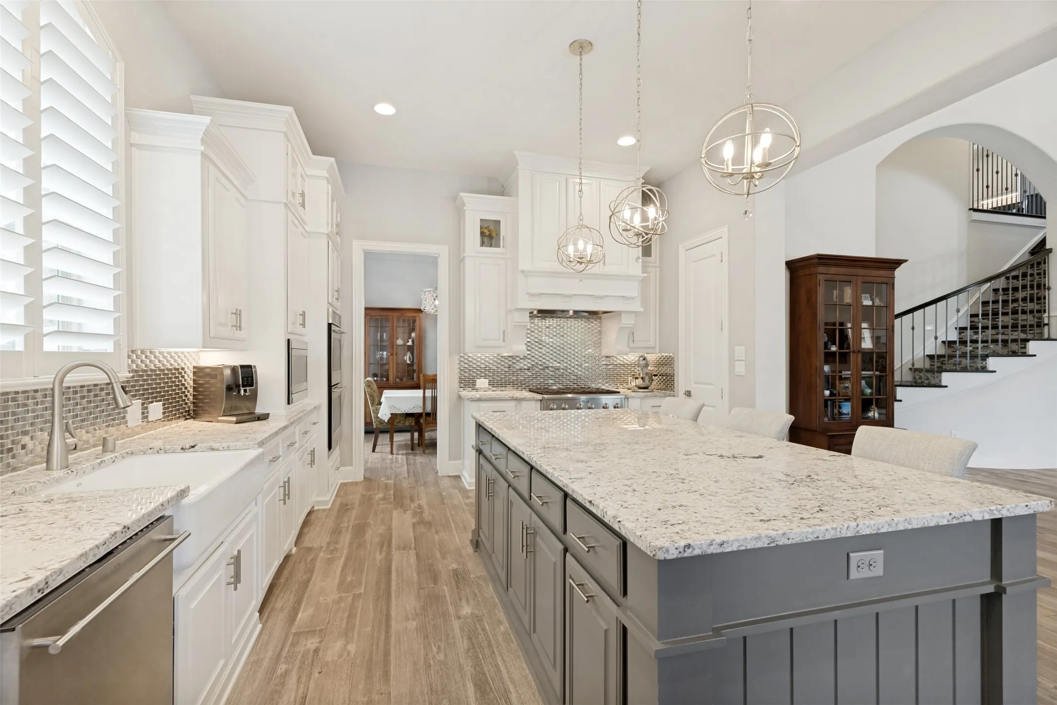 Light granite countertops capture the colors in the cabinets, island, backsplash and durable Luxury Vinyl Flooring beautifully. A white farm sink and stainless dishwasher are in the cabinets below a window with shutters, and the island holds a trash drawer.  Direct access to the formal dining room makes serving easy.