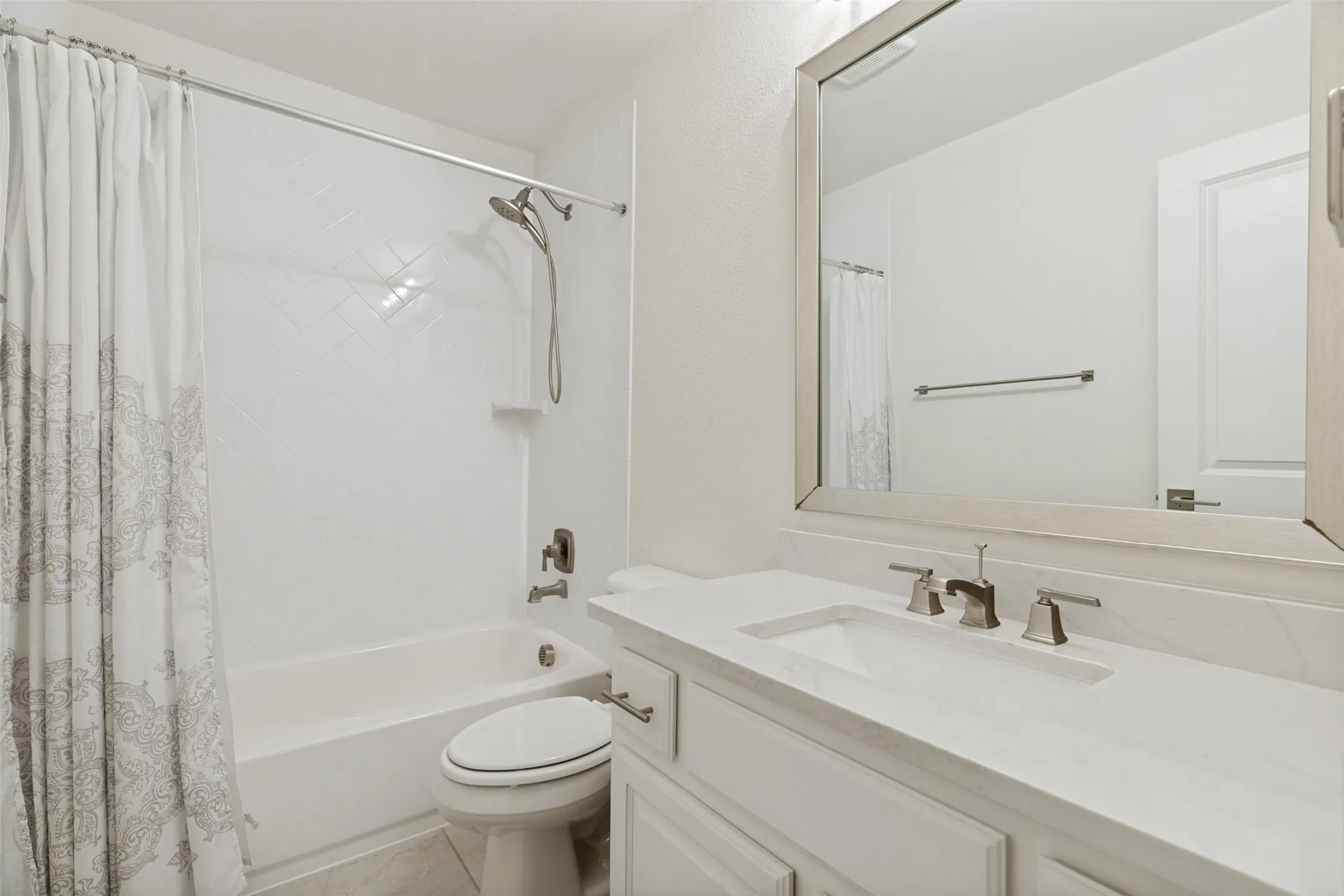All bedrooms in the home have en-suite baths.  Two of the upstairs baths have exactly the same features as shown here.  White vanity cabinets have a framed mirror above and light on top.  Ceramic tile is on the floor.  The tub/shower combination has a white tile enclosure with a herringbone pattern.
