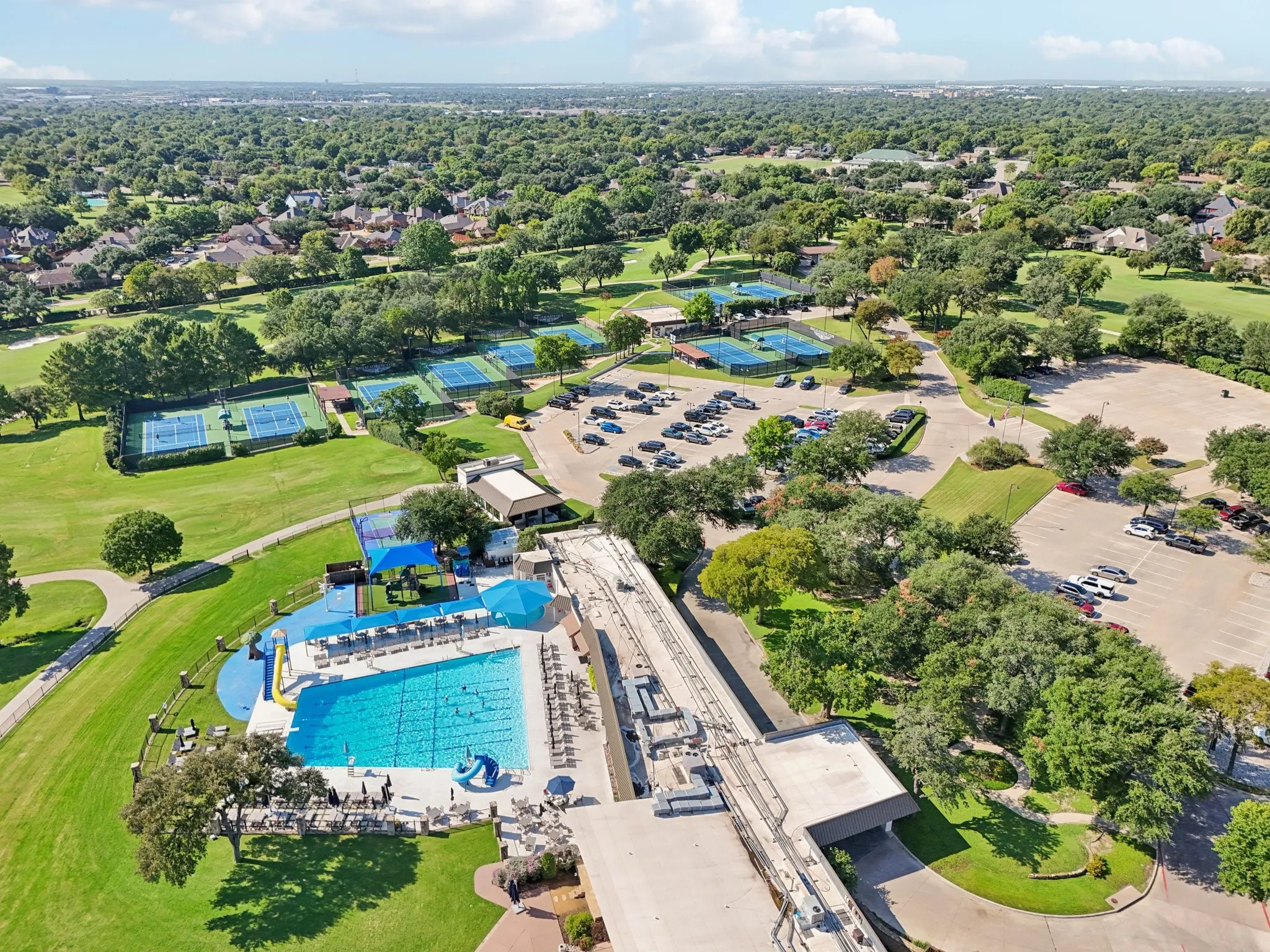 Aerial perspective showcasing extensive community amenities, including a large swimming pool, multiple tennis courts, and expansive parking areas