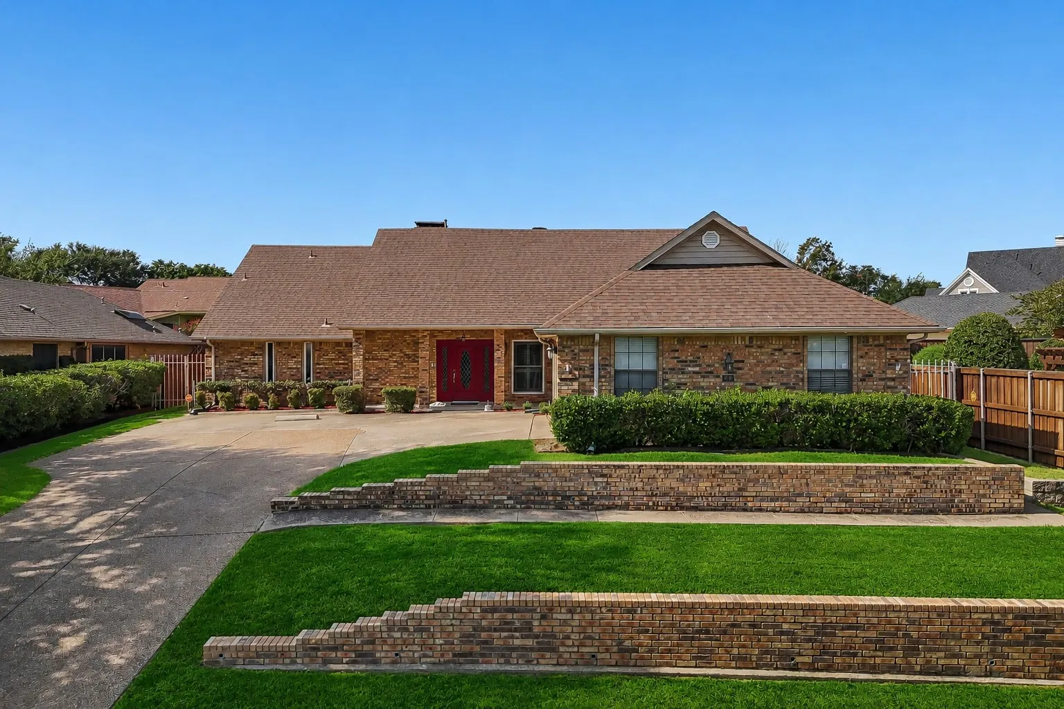 Brick-clad residence featuring a red double-door entry, a brown shingle roof, and a concrete driveway