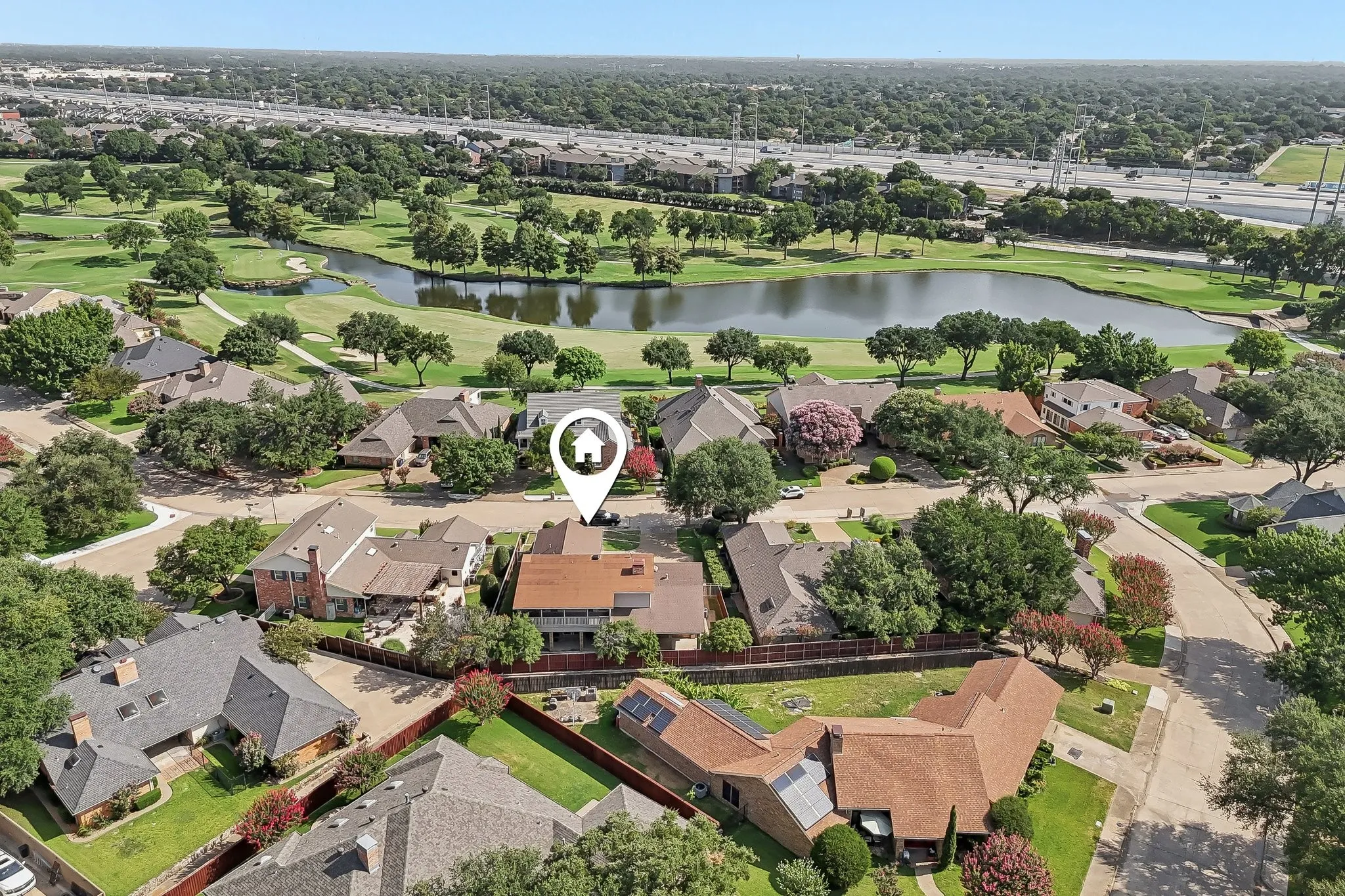 Aerial view showcasing the property within a residential community, featuring mature trees and a golf course with a prominent pond