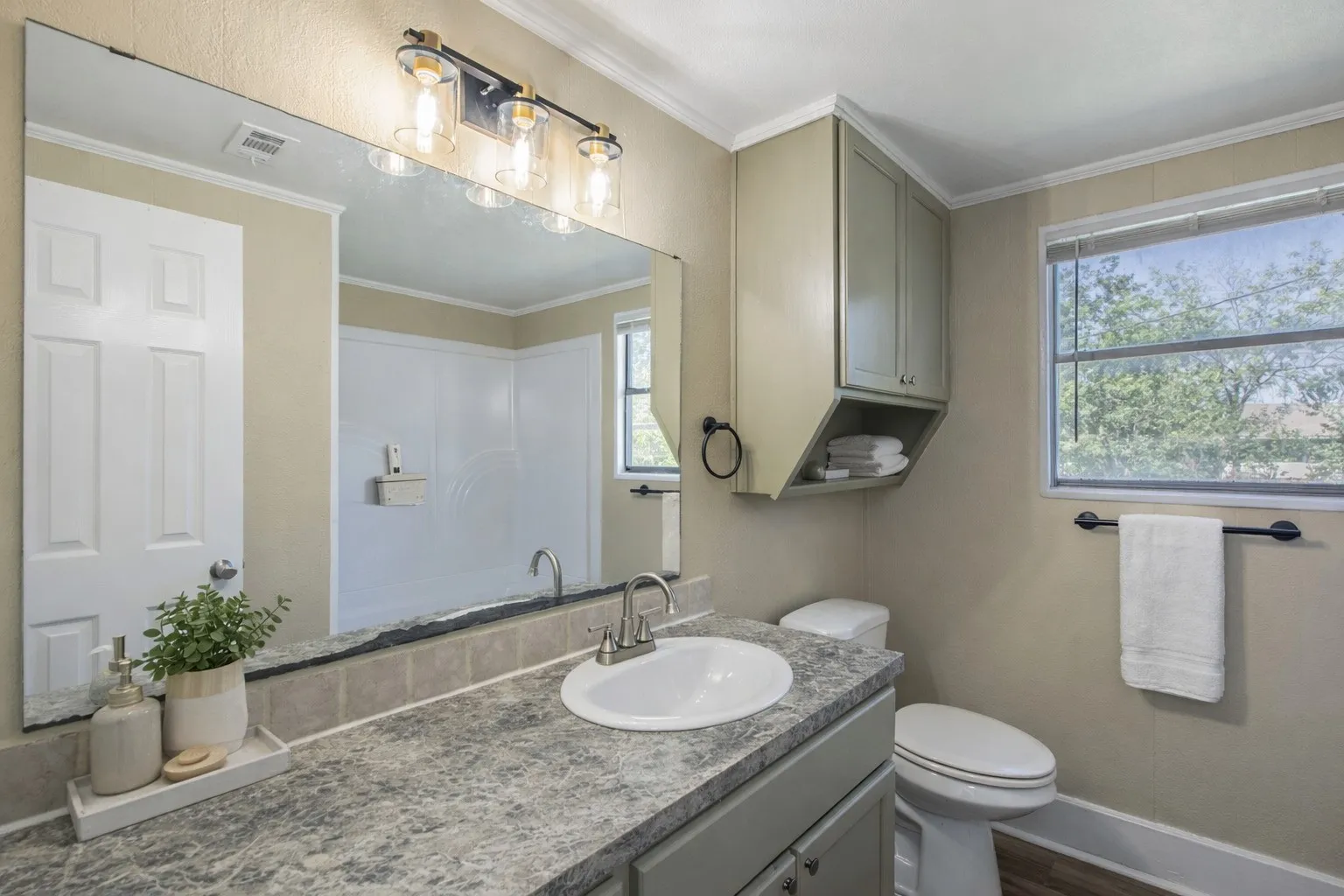 Bathroom featuring a vanity with a white basin sink and stone-look countertop, ample mirror, and overhead cabinet storageAi Staged.