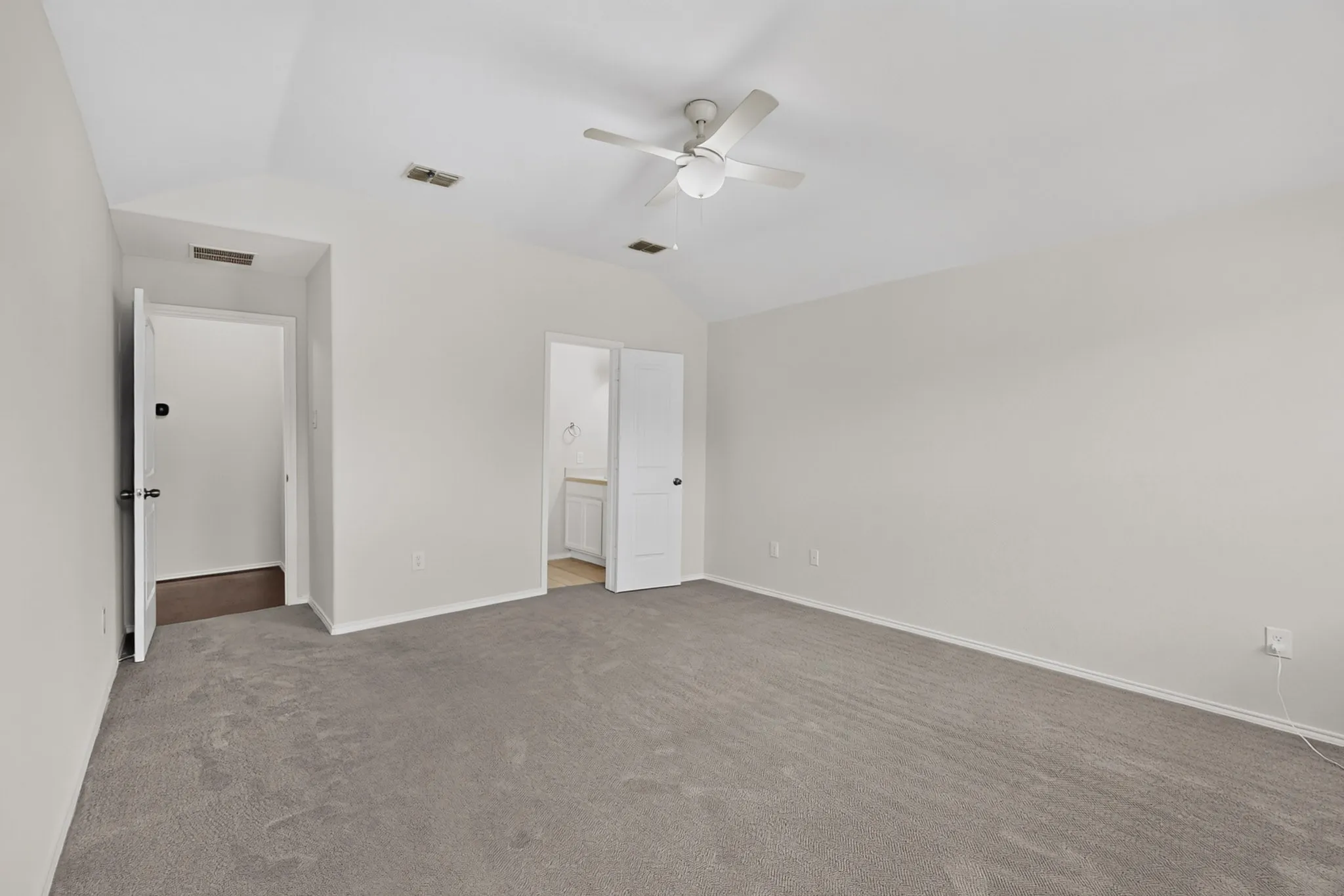 Vaulted ceiling with an attached ceiling fan, light gray carpeting, and white walls