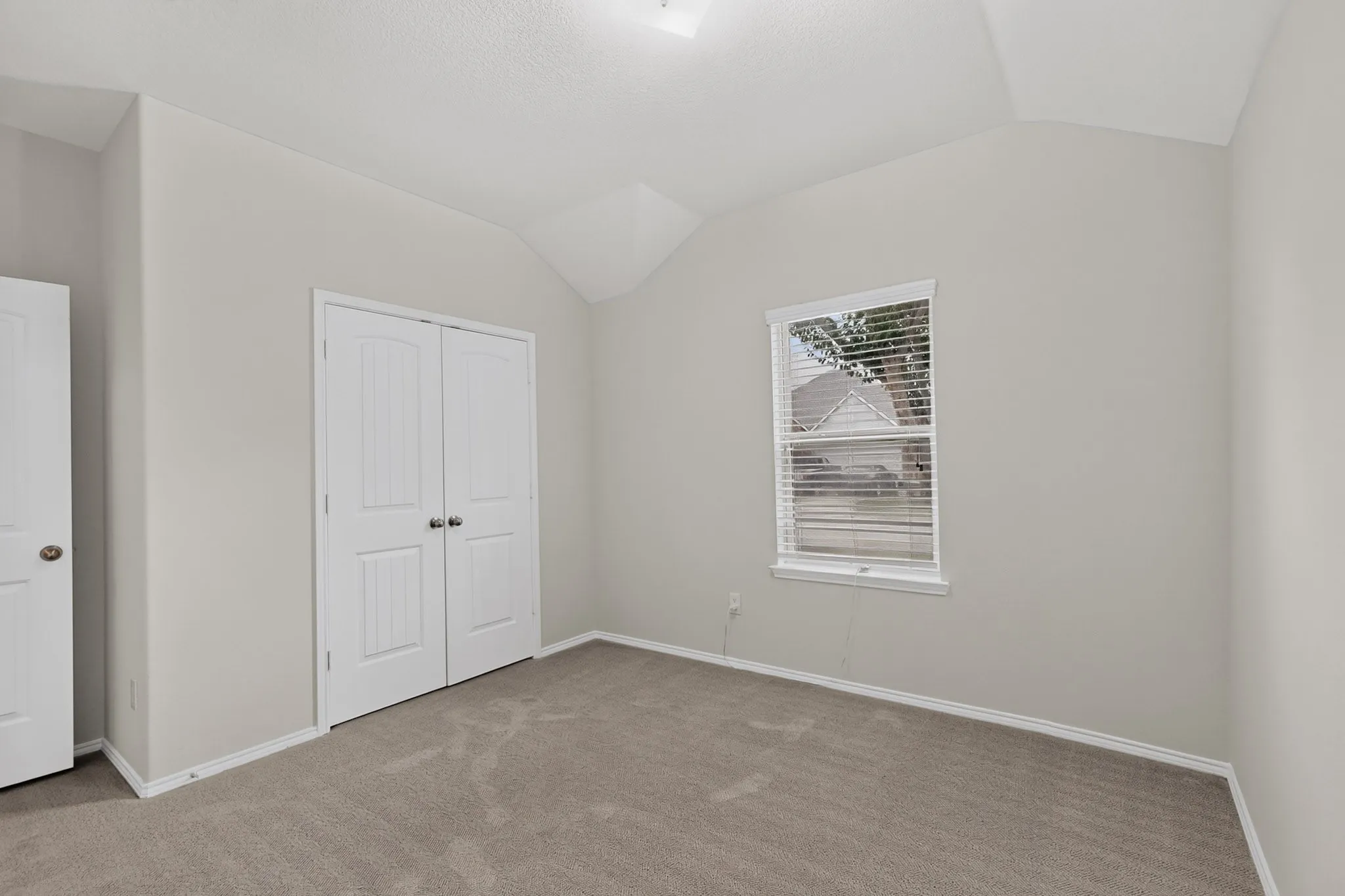 Vaulted ceiling, neutral wall paint, carpeted flooring, window with blinds, paneled doors