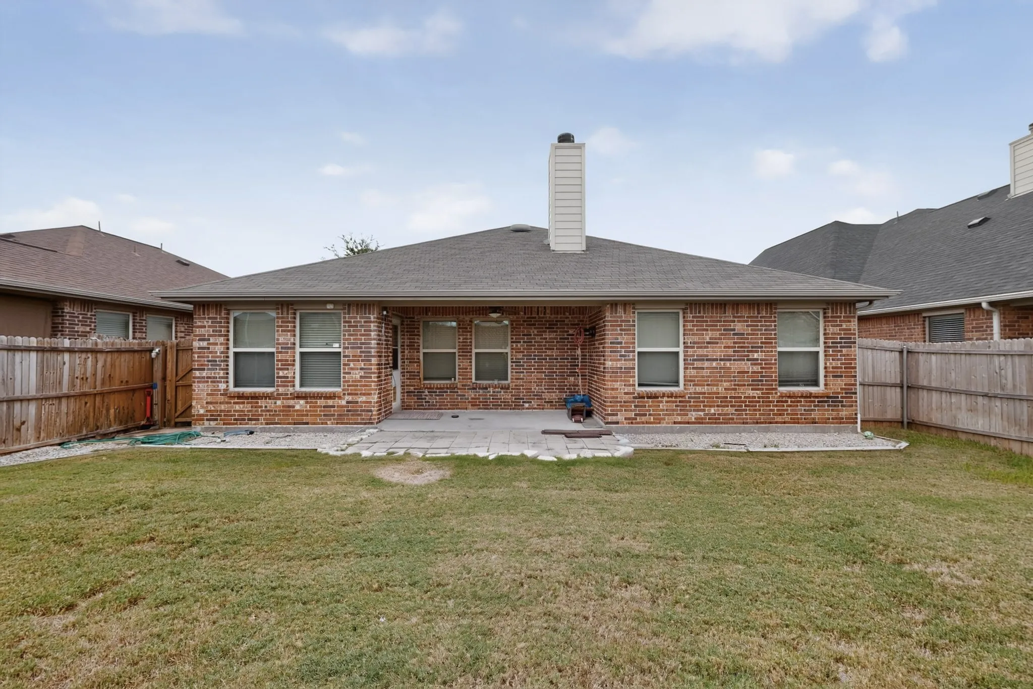 Brick exterior with a covered patio, multiple windows, and a paved outdoor area