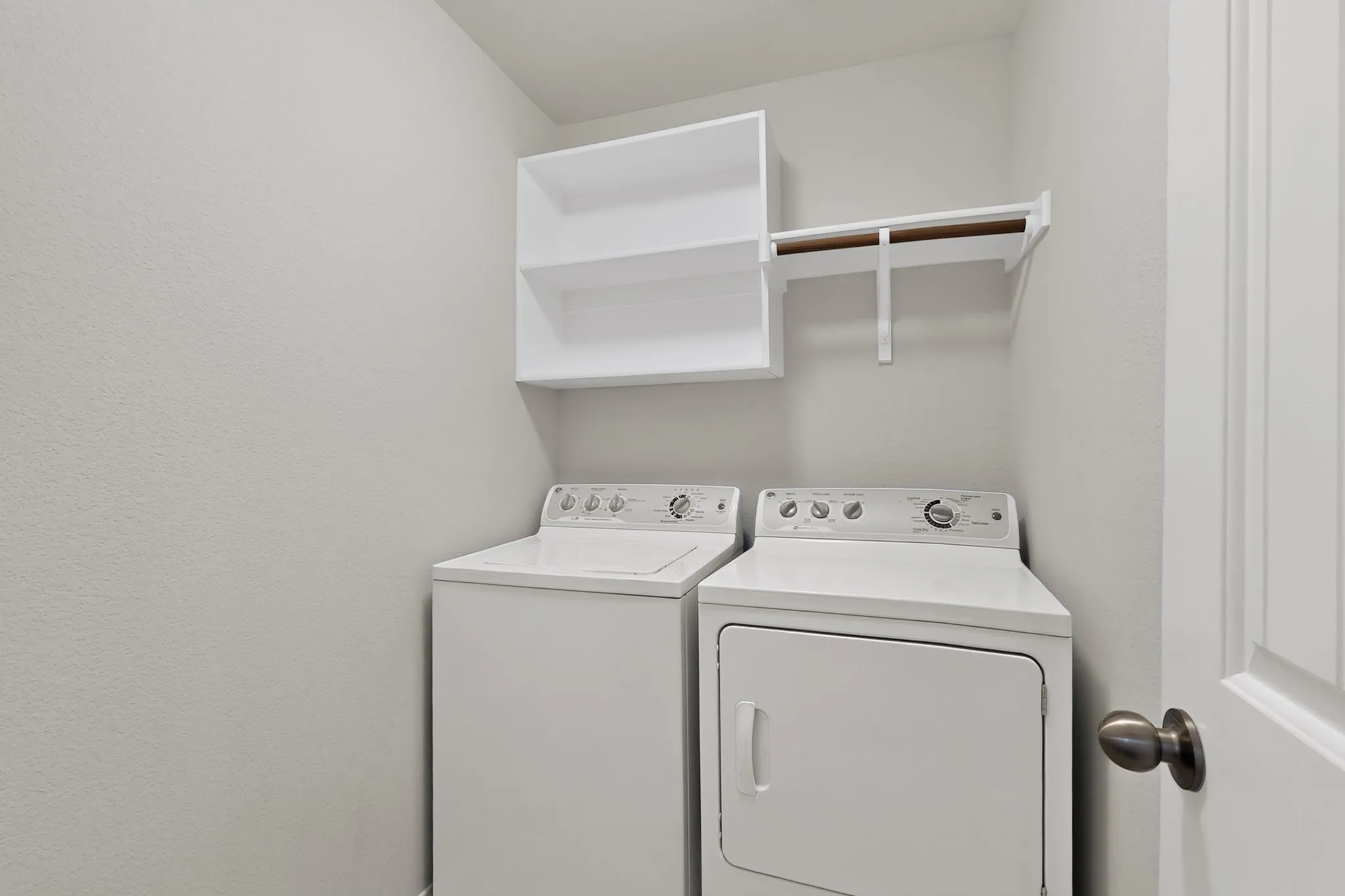 Laundry area featuring a top-load washer, front-load dryer, and upper shelving with a hanging rod