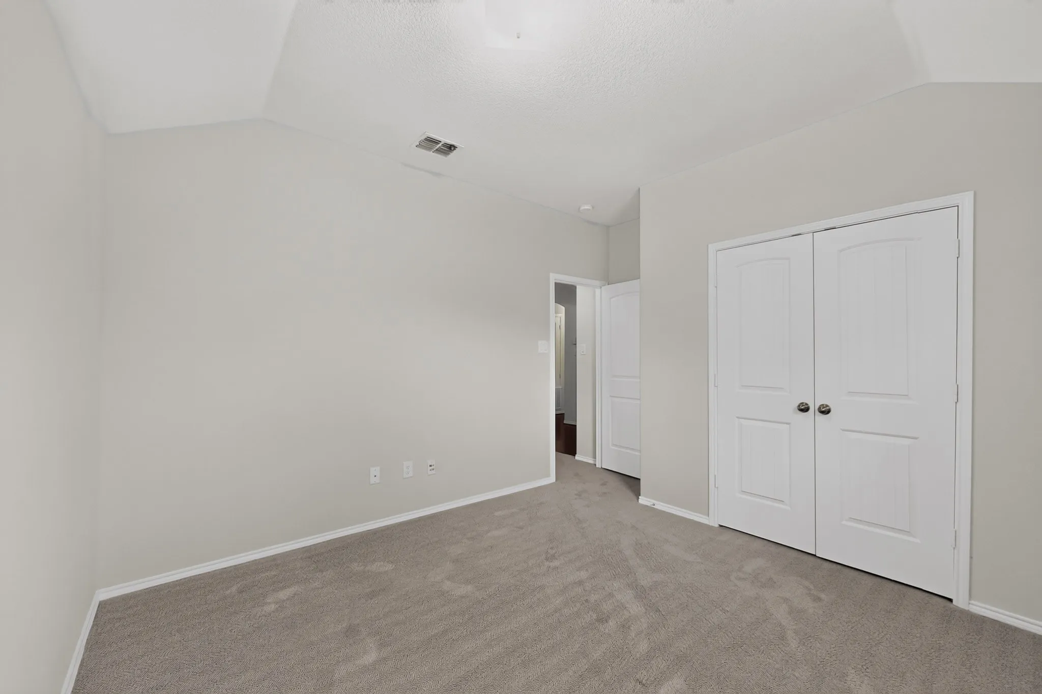 Vaulted ceiling, neutral tone carpet, white painted walls, white bi-fold closet doors, and a white trim package