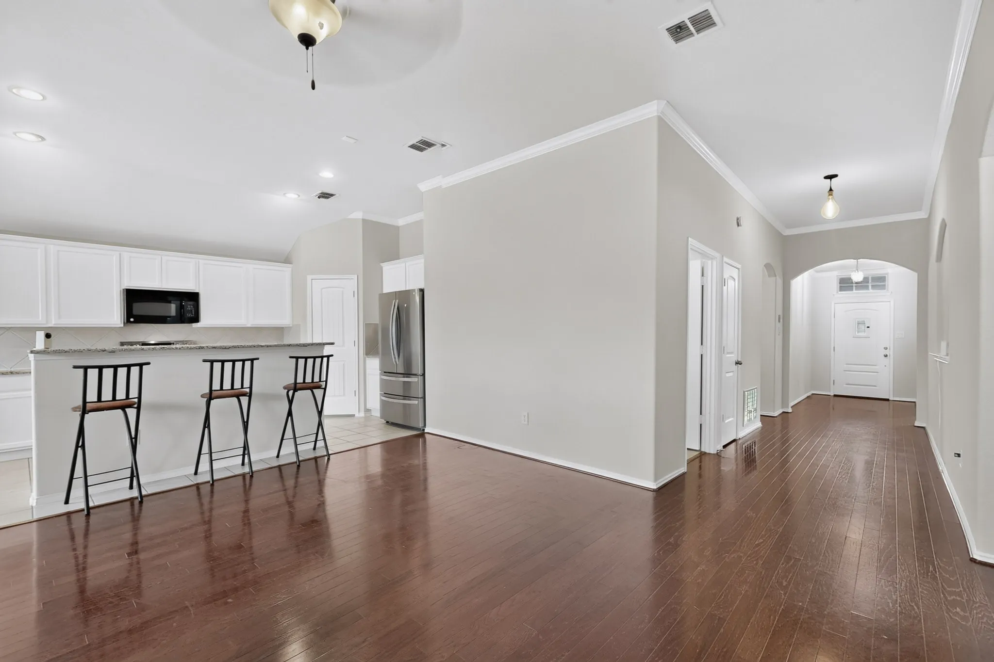 Hardwood-style flooring throughout, white kitchen cabinetry, stainless steel refrigerator, recessed lighting, and crown molding