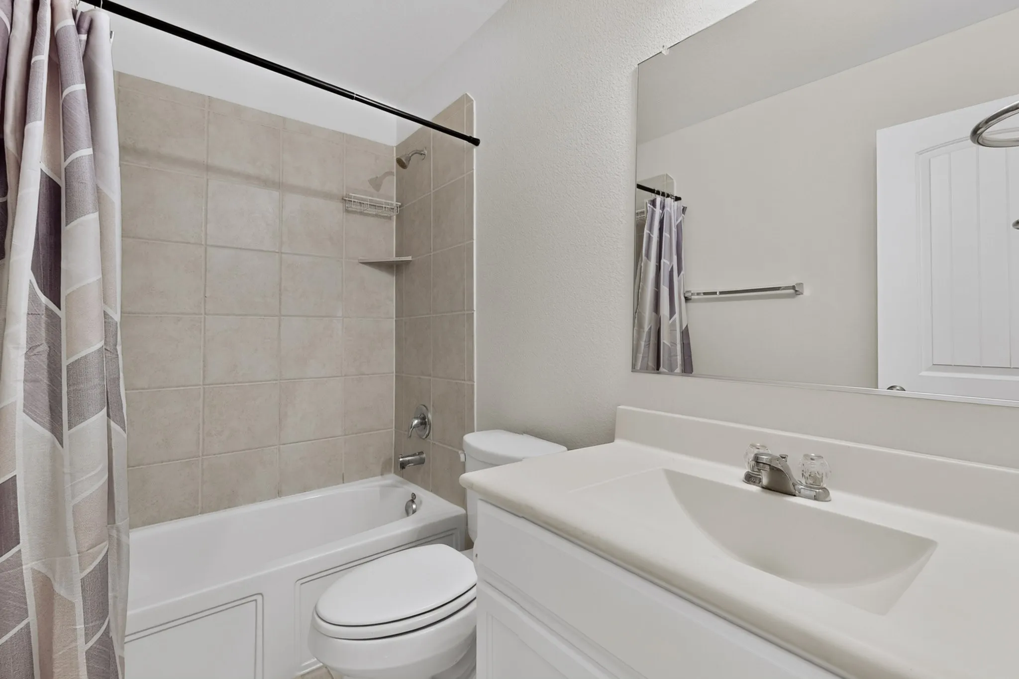 White bathtub with an integrated shower, tiled surround, and built-in shelf