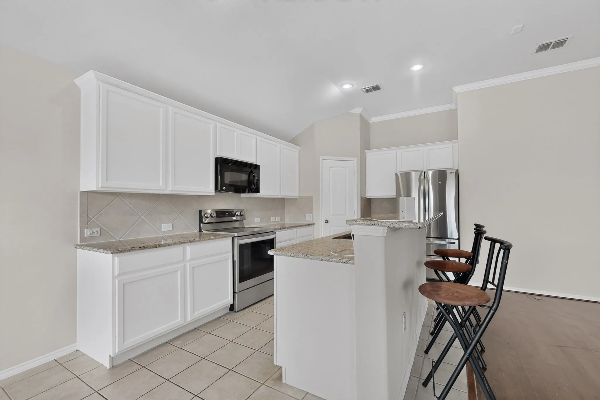 Kitchen featuring white cabinetry, light-toned tile flooring, light-toned backsplash, stainless steel appliances, and a breakfast bar