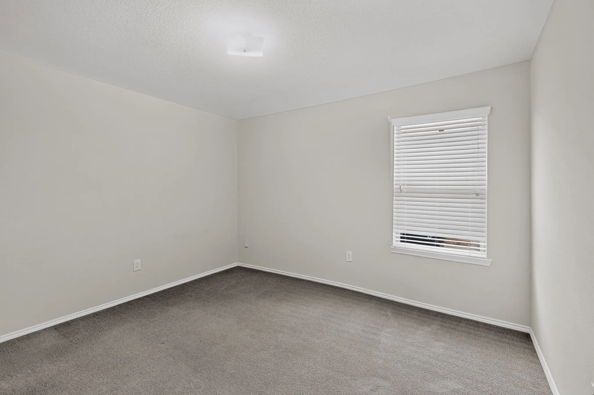 Bright corner bedroom with neutral wall finishes, recessed ceiling lighting, and large window with plantation shutters providing natural light and privacy control