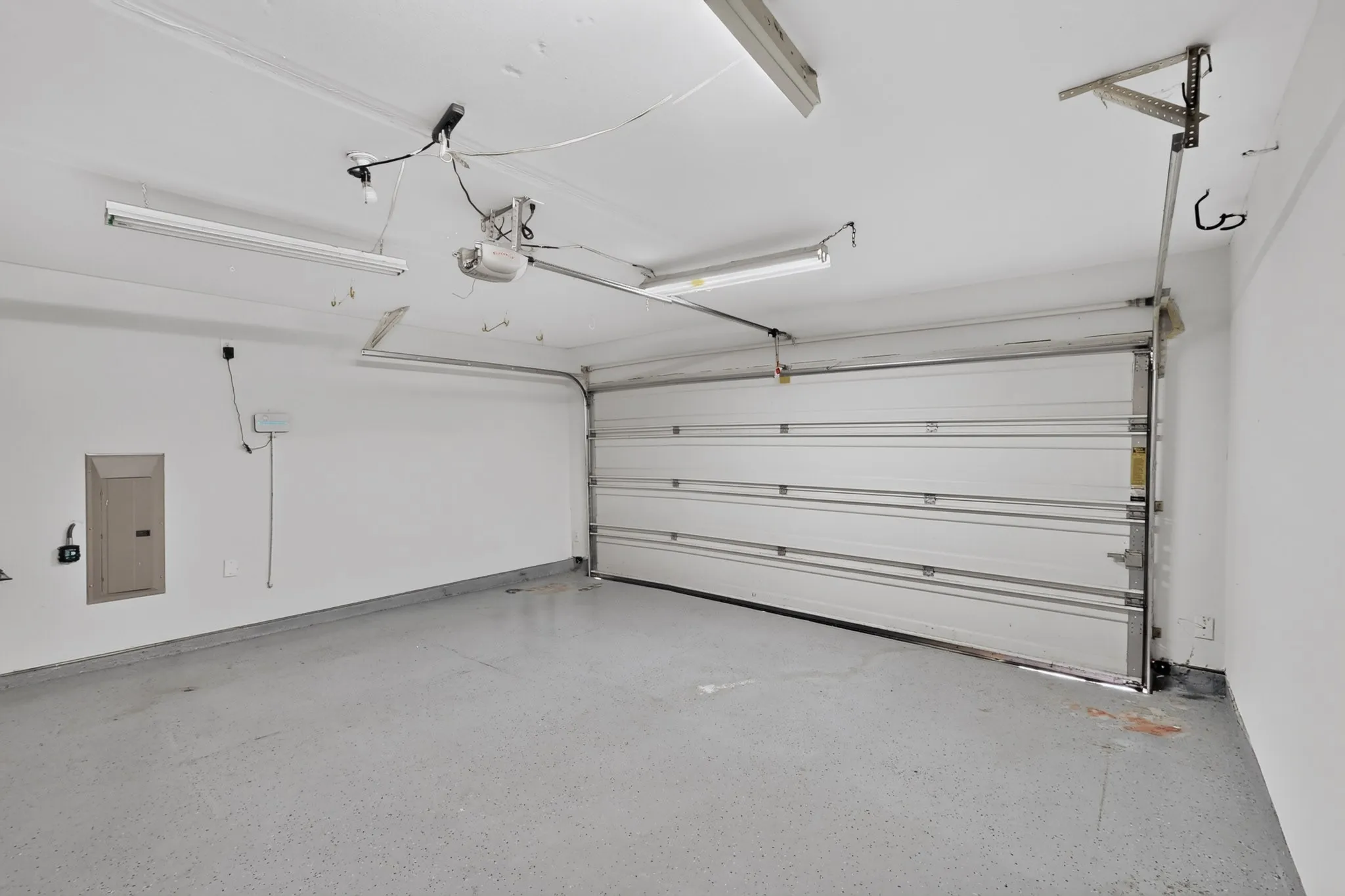 Garage space featuring a speckled concrete floor, white walls, and an overhead garage door