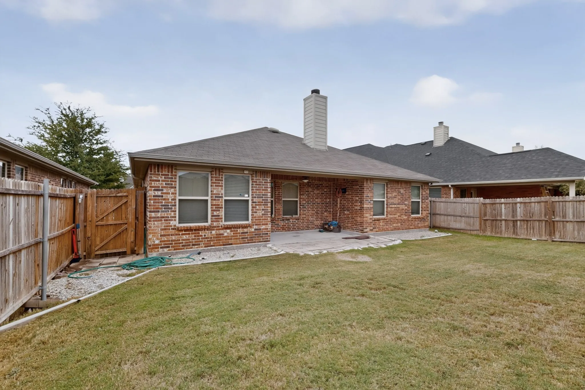 Brick exterior featuring a covered patio with a stone-finish surface, a substantial grass area, and wood fencing