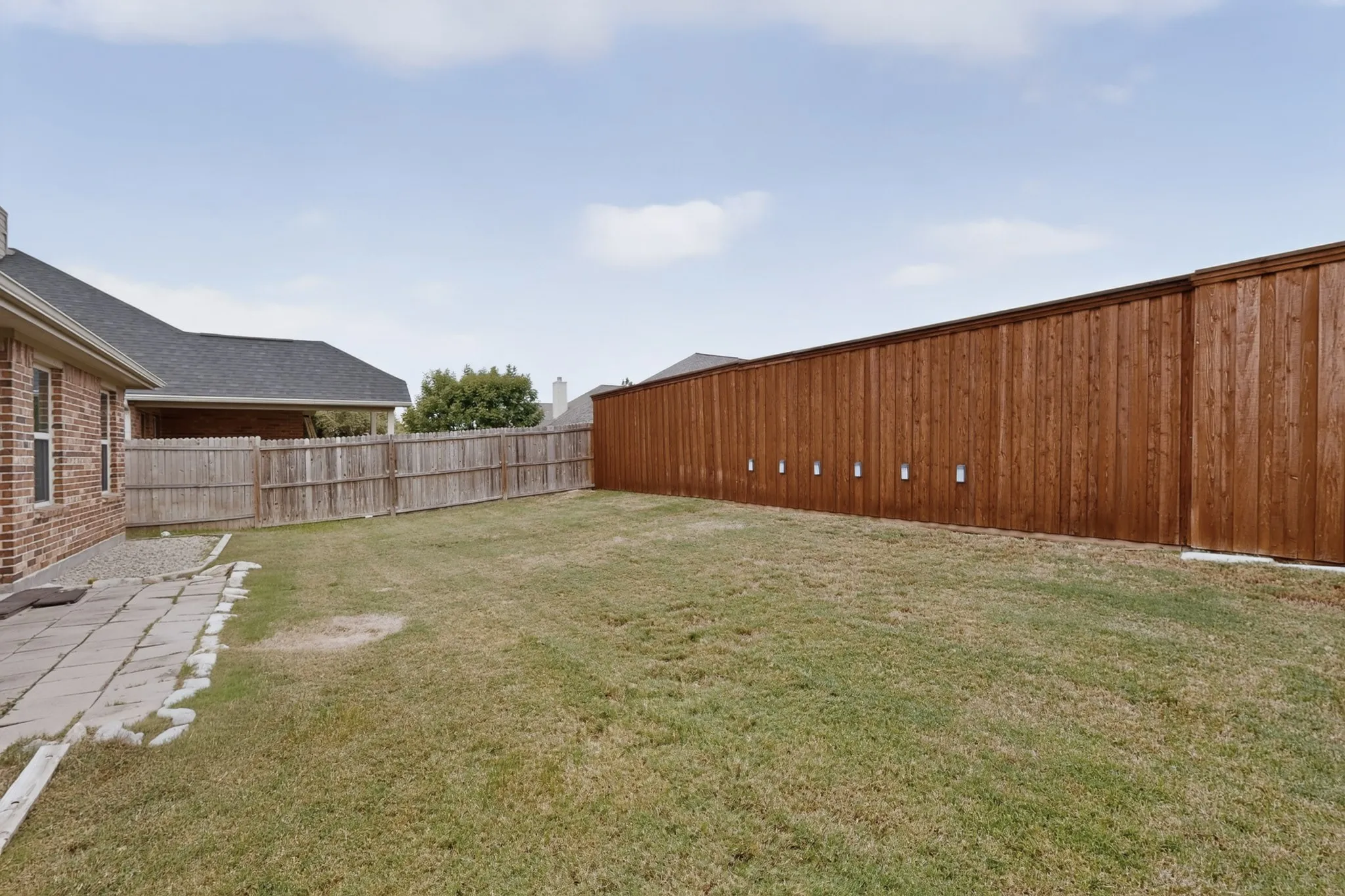 Expansive rear yard featuring a large grass area, a partial paver patio, and a new privacy fence