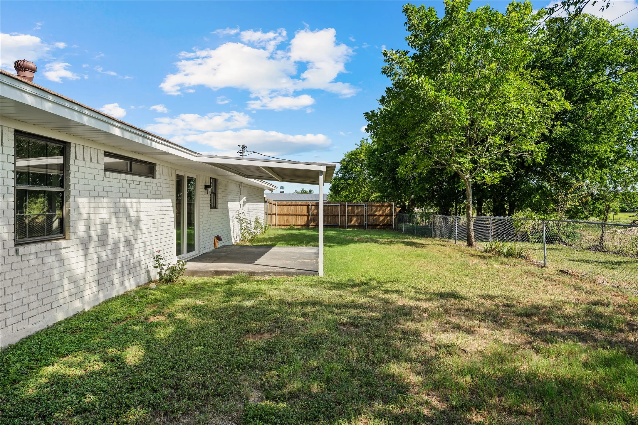 Expansive backyard featuring a mature tree, chain-link fencing, and a wooden privacy fence