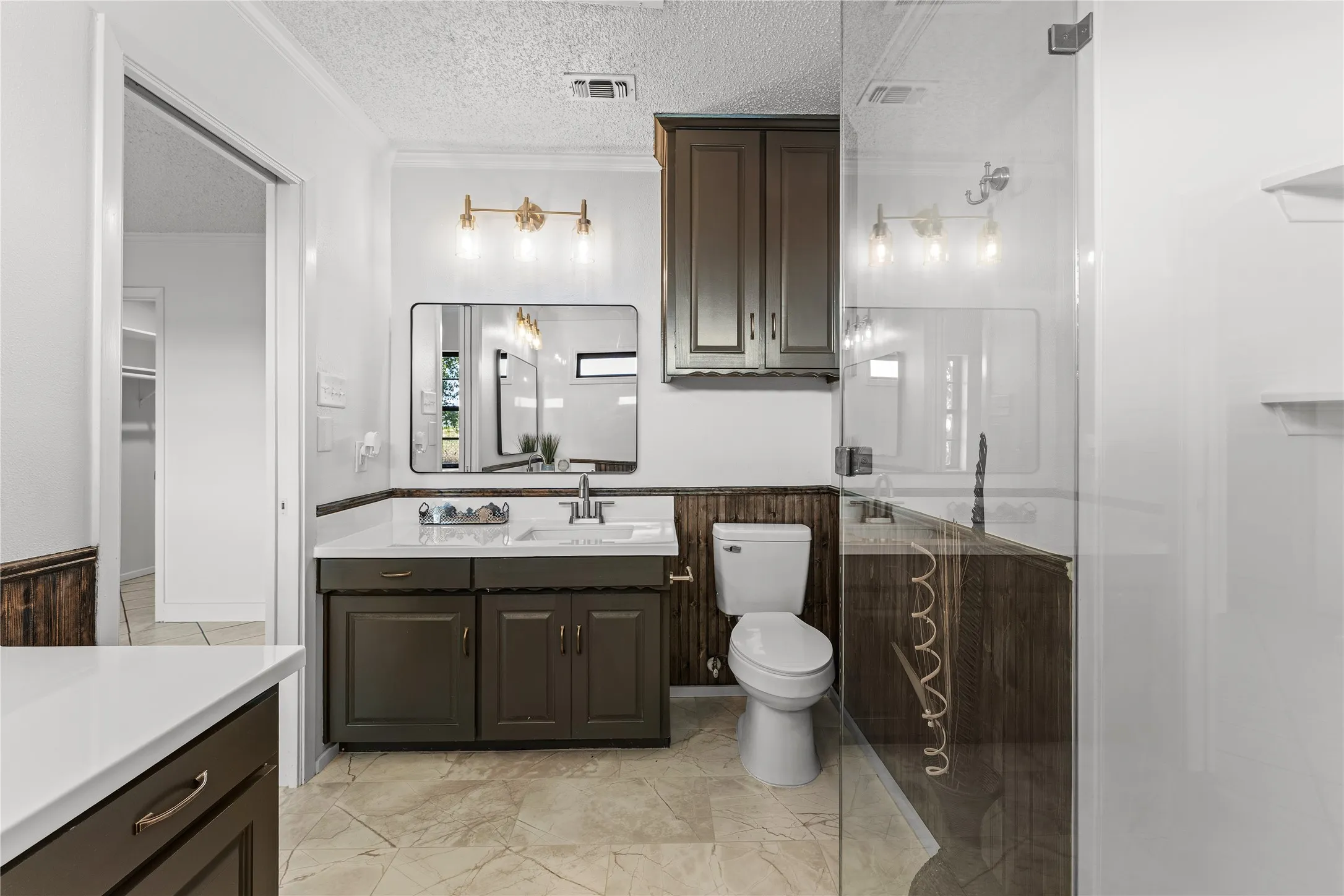 Bathroom featuring a single vanity with dark cabinetry and white countertop, a rectangular framed mirror, a toilet, and a glass-enclosed shower
