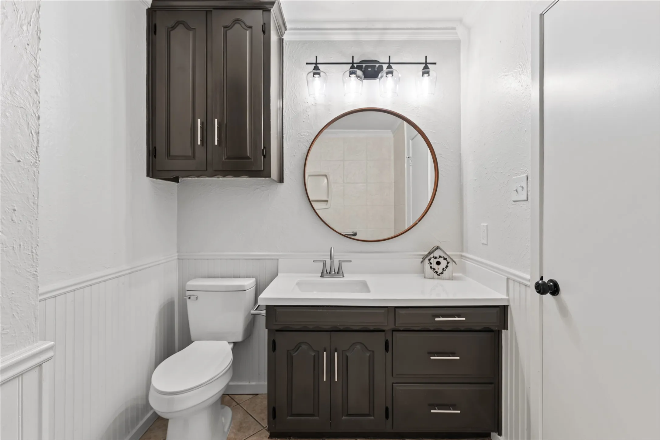 Modern bathroom vanity with a white countertop and rectangular sink, complemented by a round mirror and overhead four-light fixture
