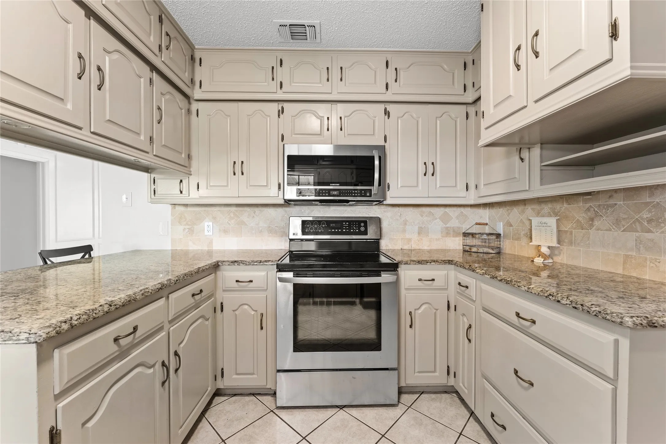 U-shaped kitchen featuring light-toned cabinetry, granite countertops, stainless steel appliances, and a tiled backsplash