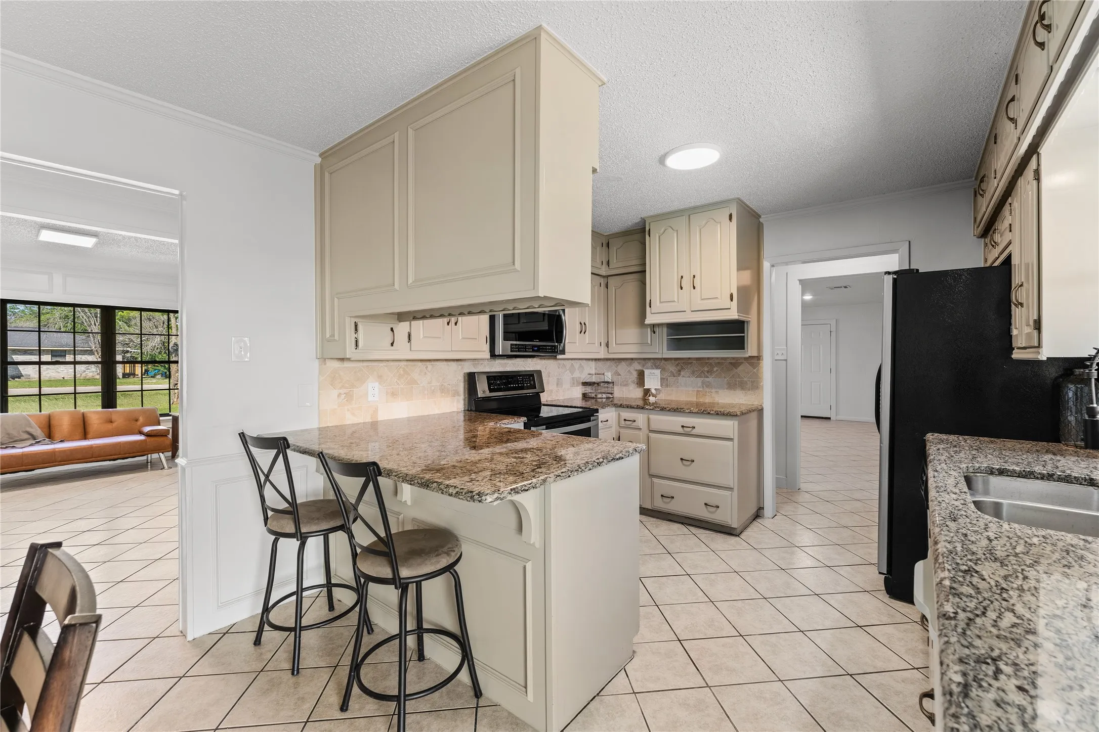 Kitchen featuring light-toned cabinetry, granite countertops, tile flooring, and integrated black appliances