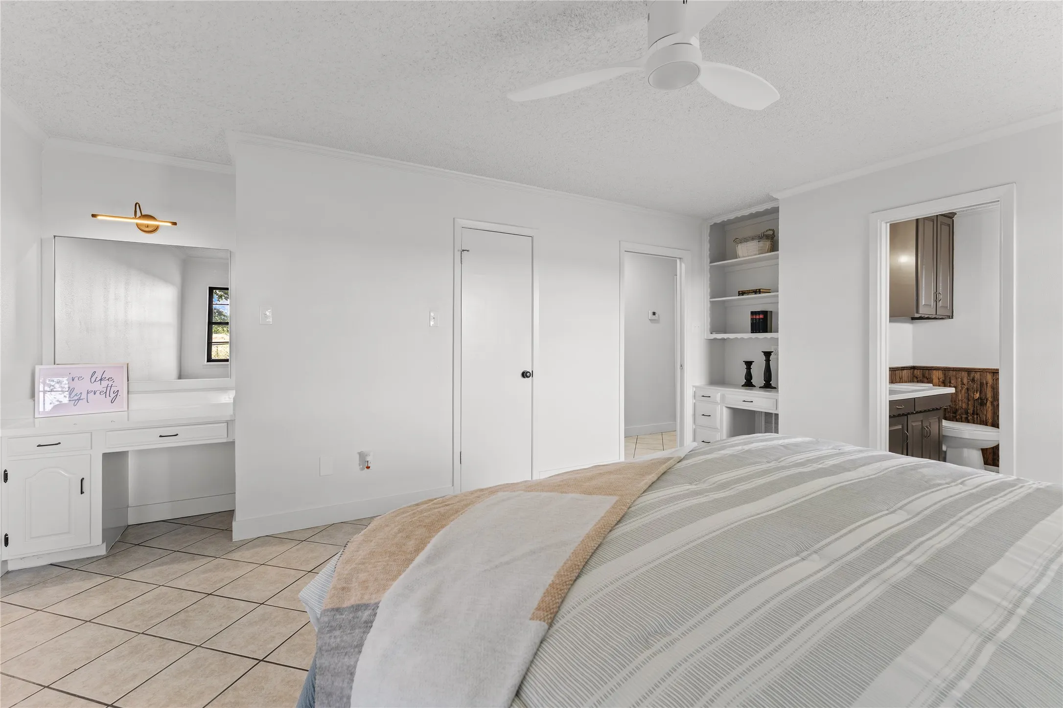 White tiled flooring throughout, featuring a built-in vanity with mirror and wall sconce