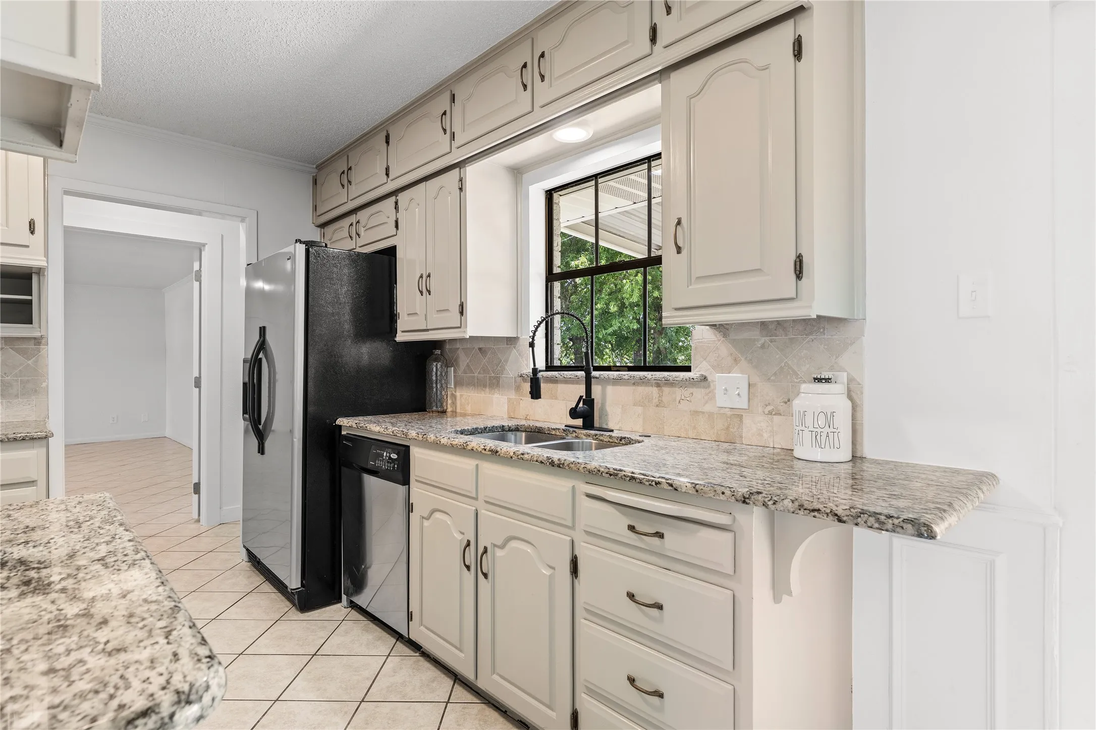 Kitchen featuring light-toned cabinetry, granite countertops, a tiled backsplash, and a black window frame