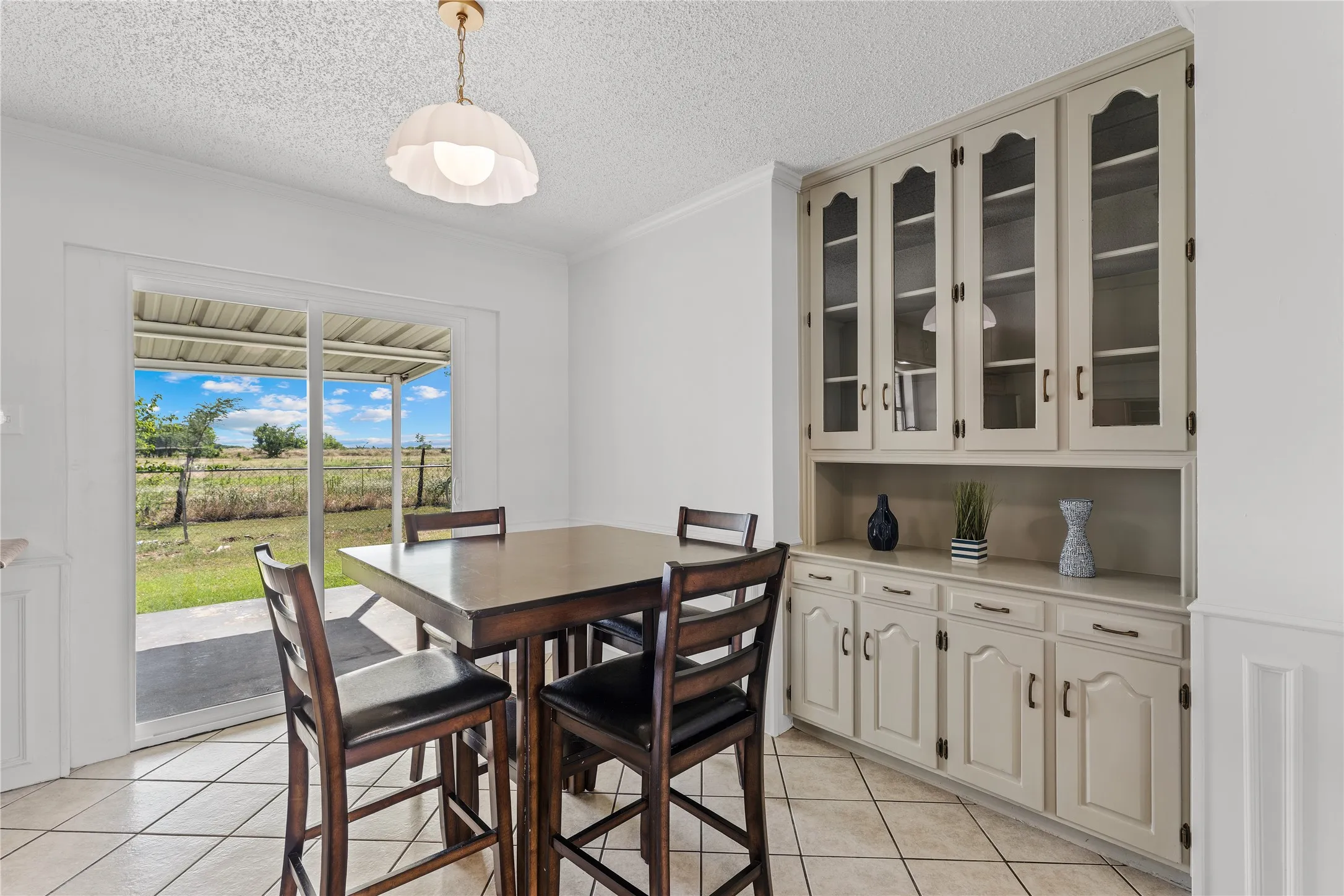 Built-in cabinetry with glass-front uppers and solid lower doors, tile flooring, and sliding glass door access to a covered patio