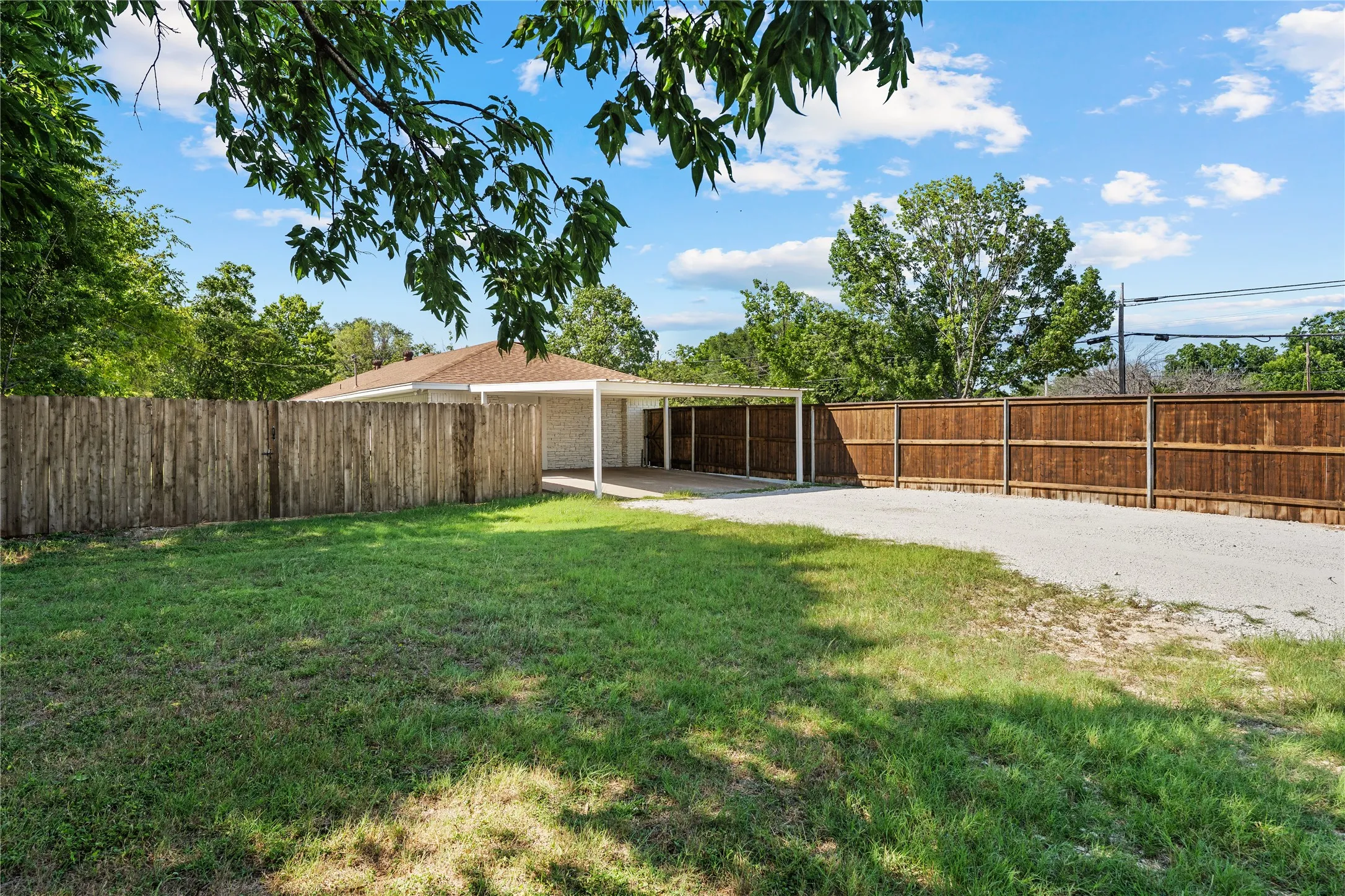 Expansive backyard featuring a lush lawn, two distinct privacy fences, and a gravel driveway