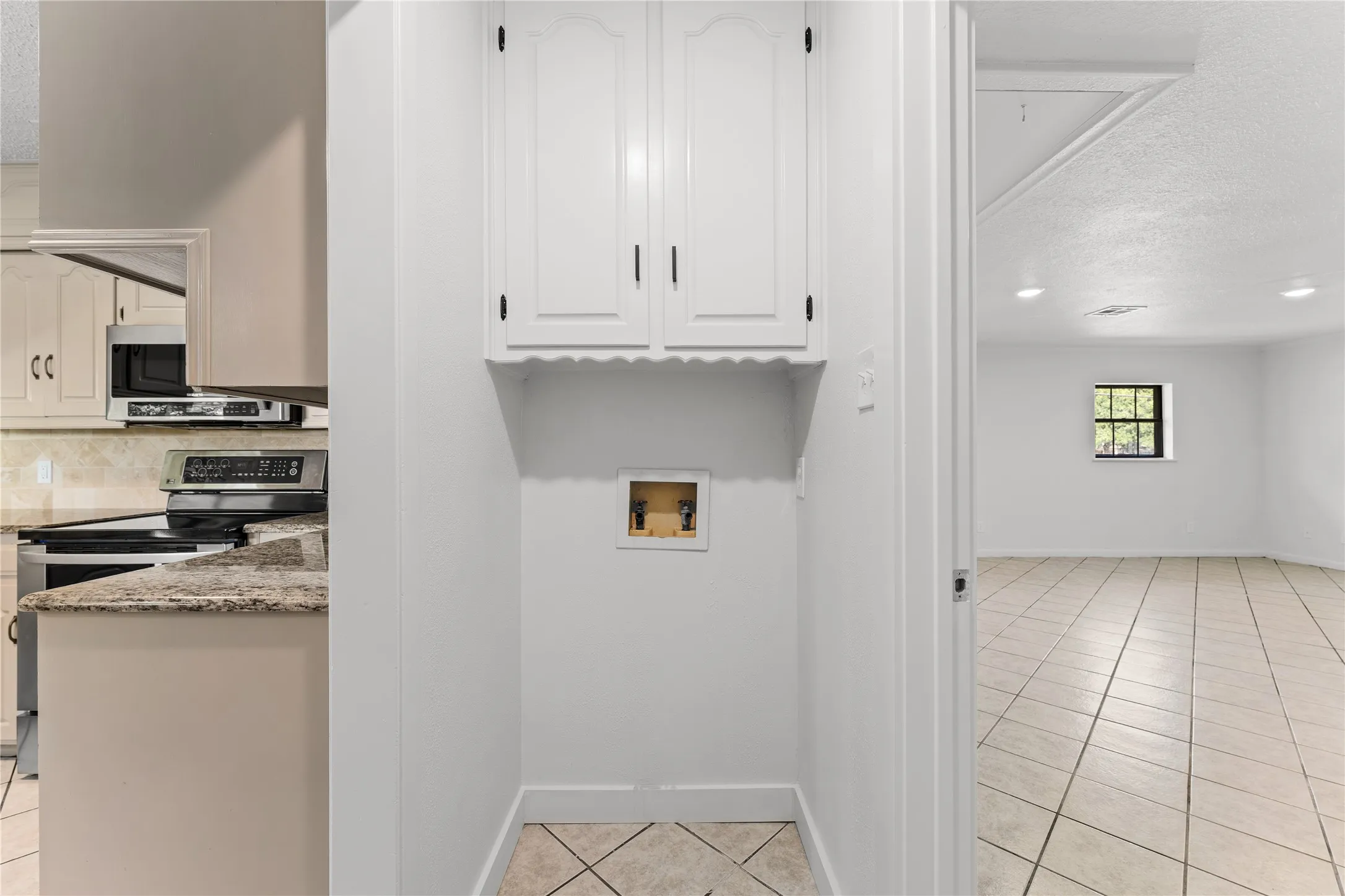 Dedicated utility area featuring white cabinetry and hookups, with tile flooring that extends into an adjacent room with a window and recessed lighting
