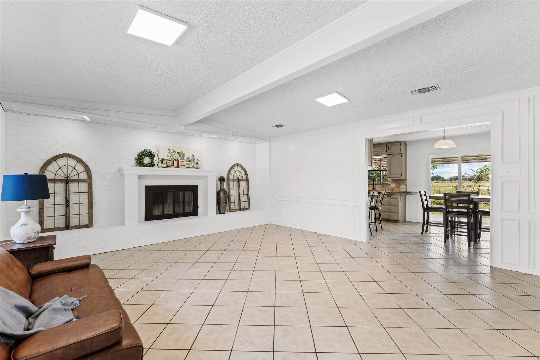 Spacious living area featuring diagonal tile flooring and a white brick fireplace with a mantel