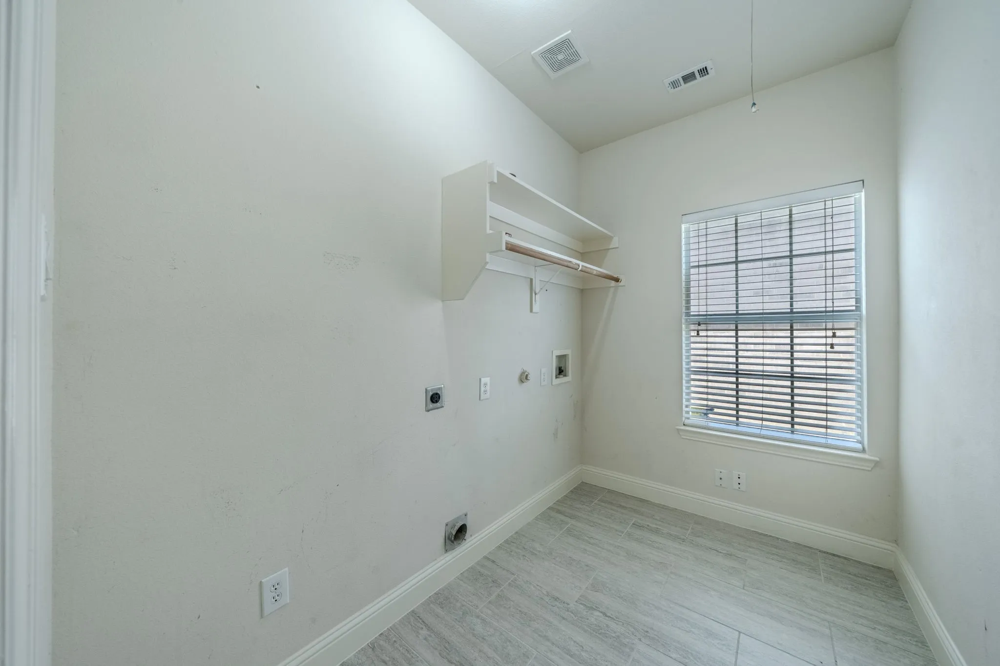 Utility room featuring light gray tile flooring, a single window with horizontal blinds, built-in shelving, and a garment rod