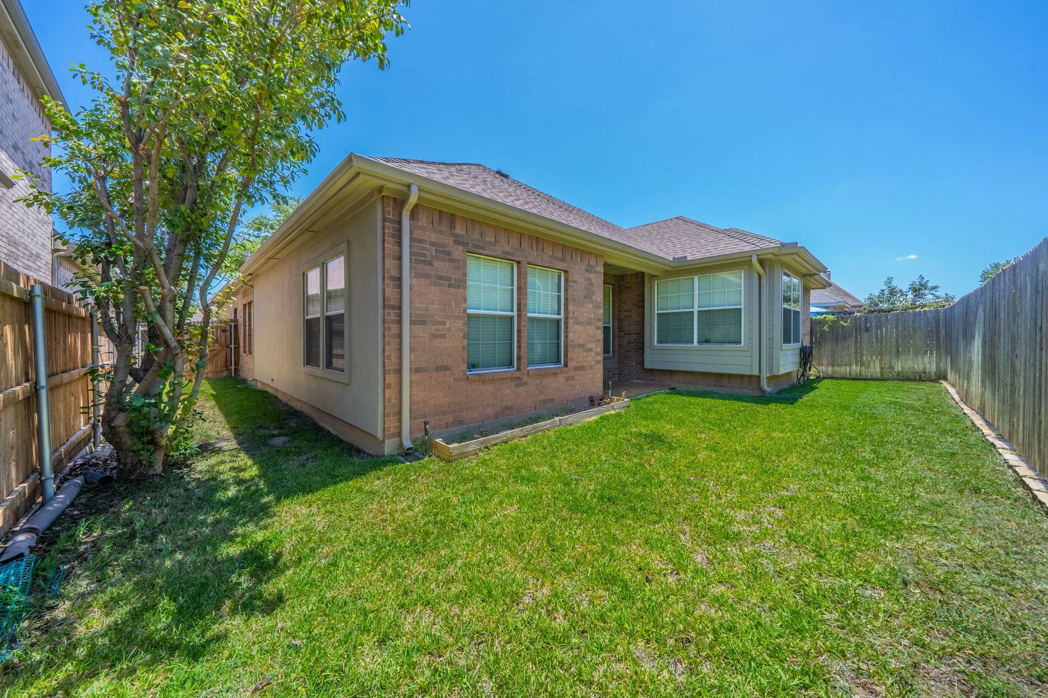 Expansive backyard featuring a manicured lawn, brick exterior, bay window, and a privacy fence